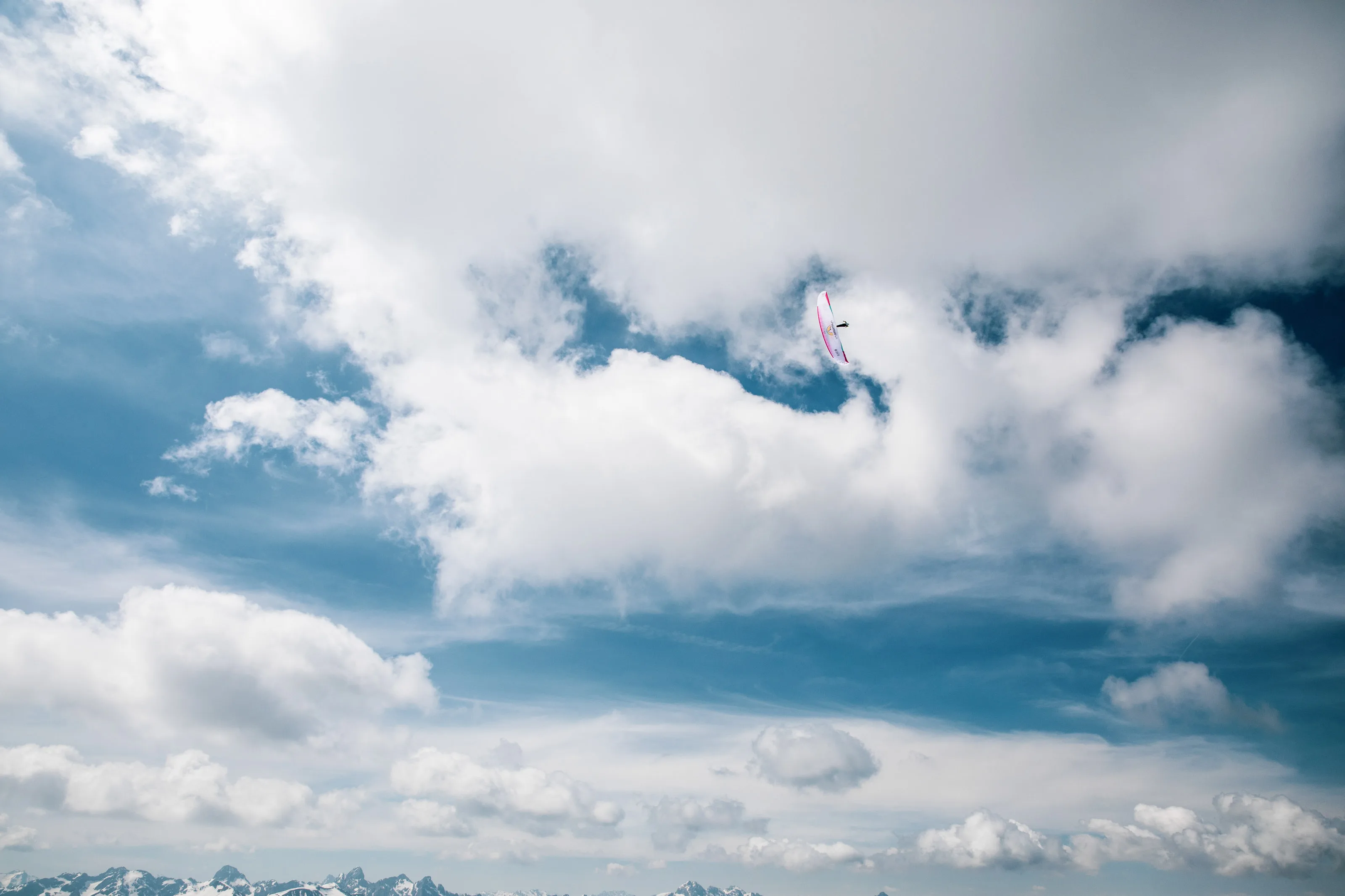 Ein pinkweißer Gleitschirm mit Michael Lacher zeichnet sich zwischen hellen Wolken und blauem Himmel ab.