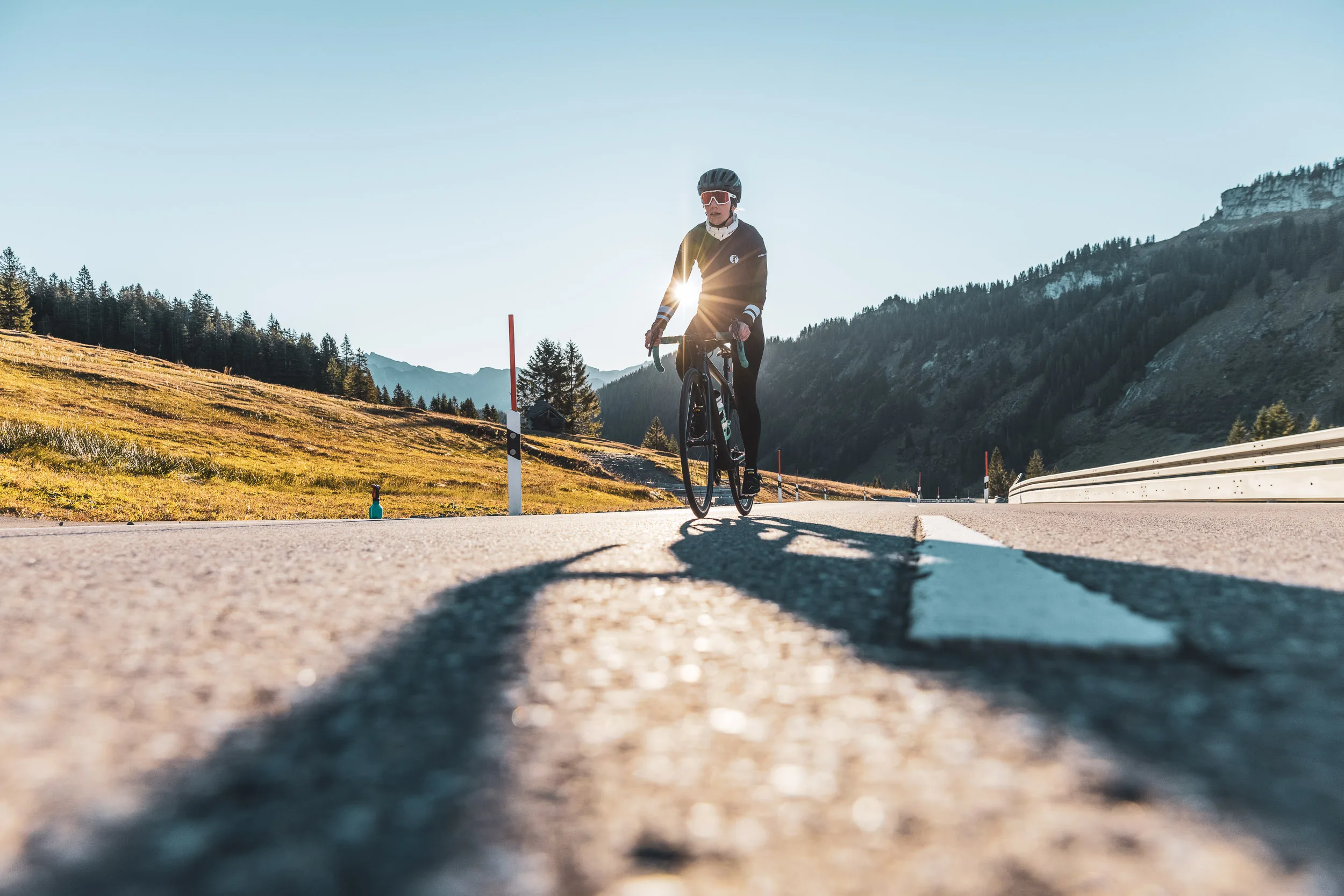 Rennradfahrerin fährt im Gegenlicht über den Riedbergpass