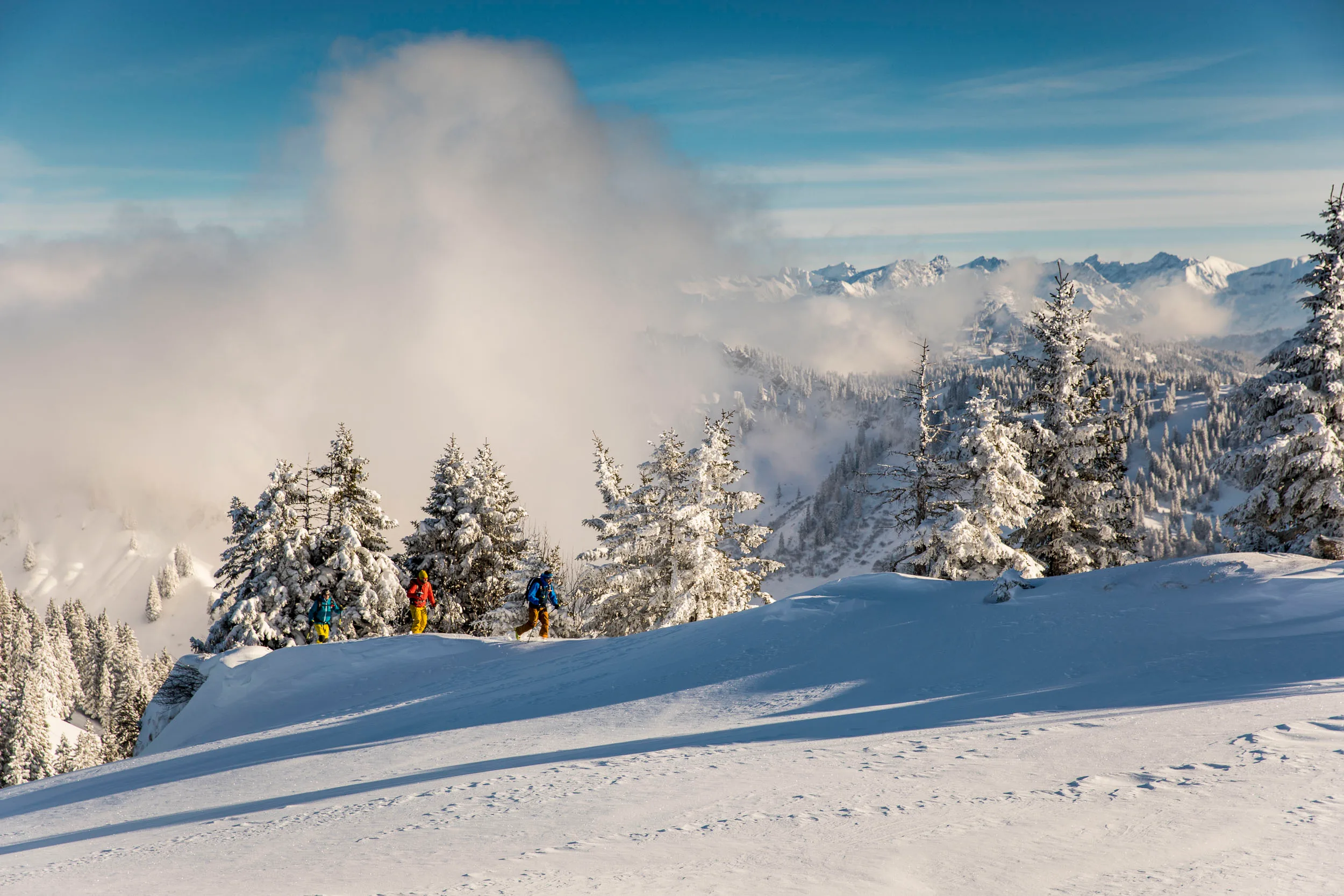 Skitourengeher folgen einer Spur über einen weiten, sonnigen Rücken.