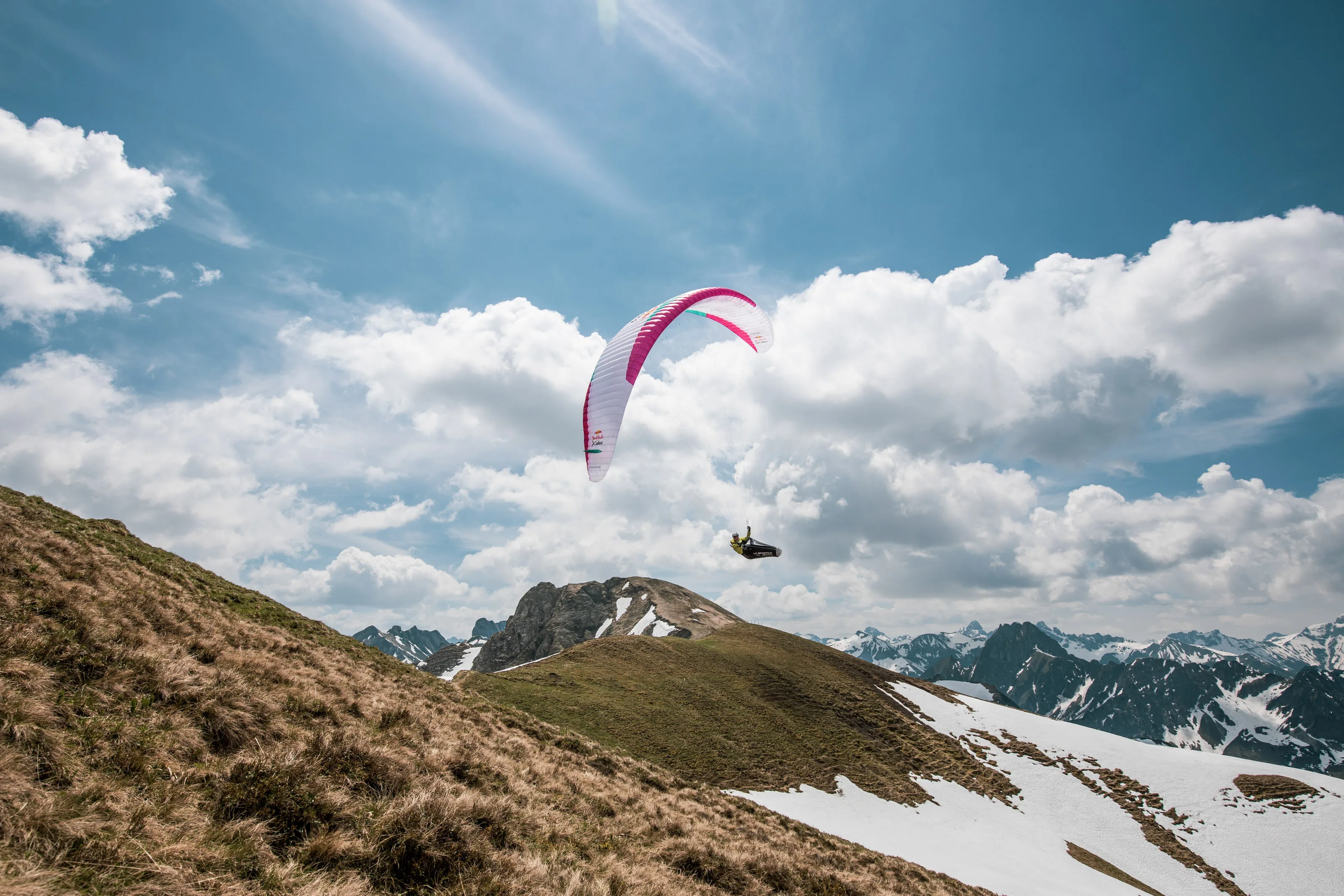 Michael Lacher entfernt sich unter dem pinkweißen Schirm über einer grasigen Bergkuppe.