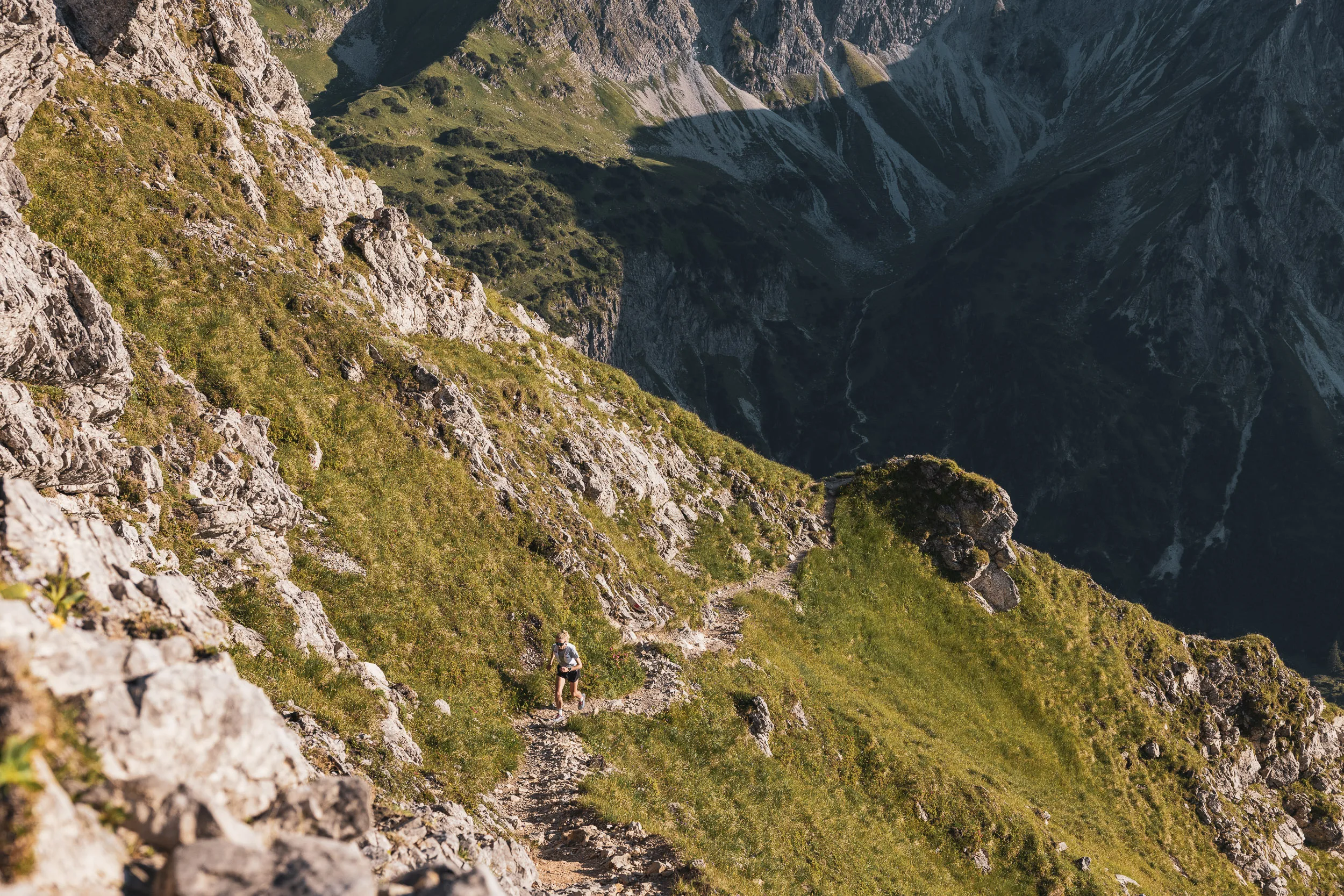 Kleine Trailrunnerin auf einem steilen Hangweg in weiter Berglandschaft