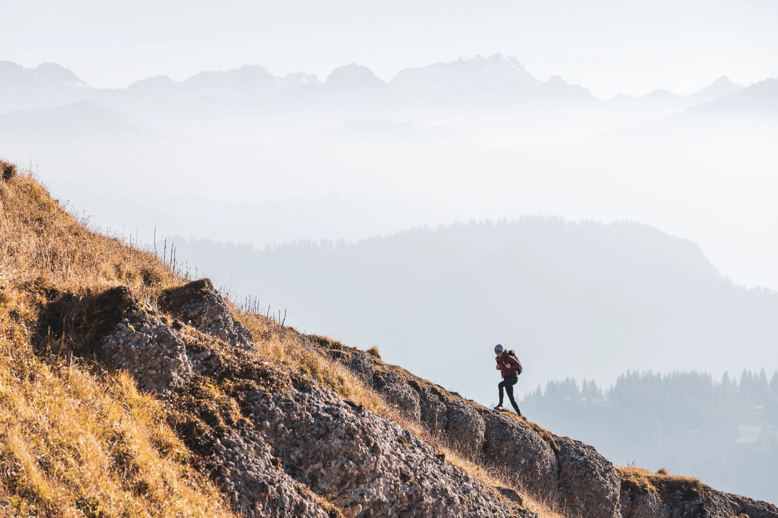 Wanderin steigt über einen schmalen Hang vor gestaffelten Bergsilhouetten auf
