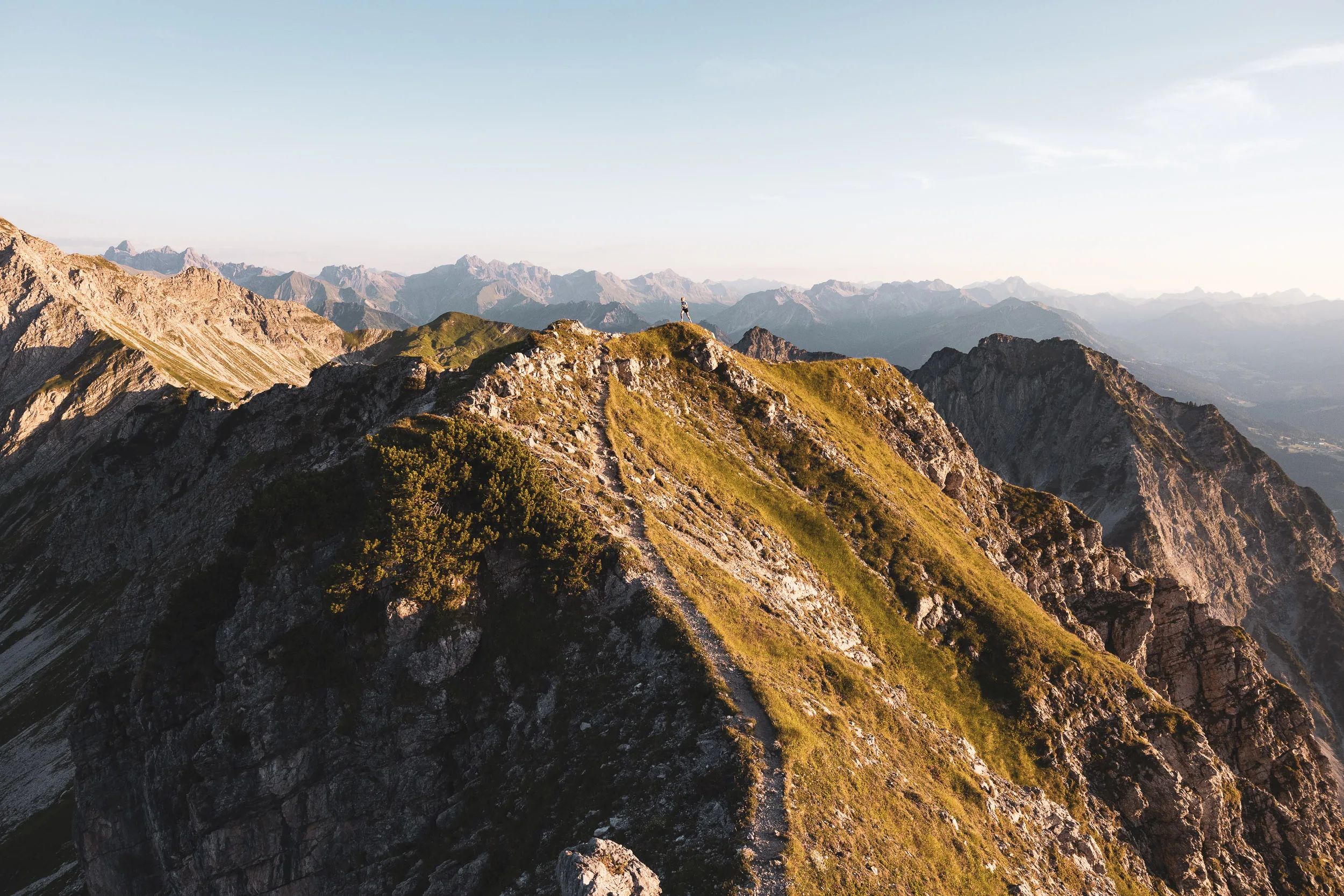 Schmaler Berggrat im warmen Licht mit weitem Blick über die Alpen