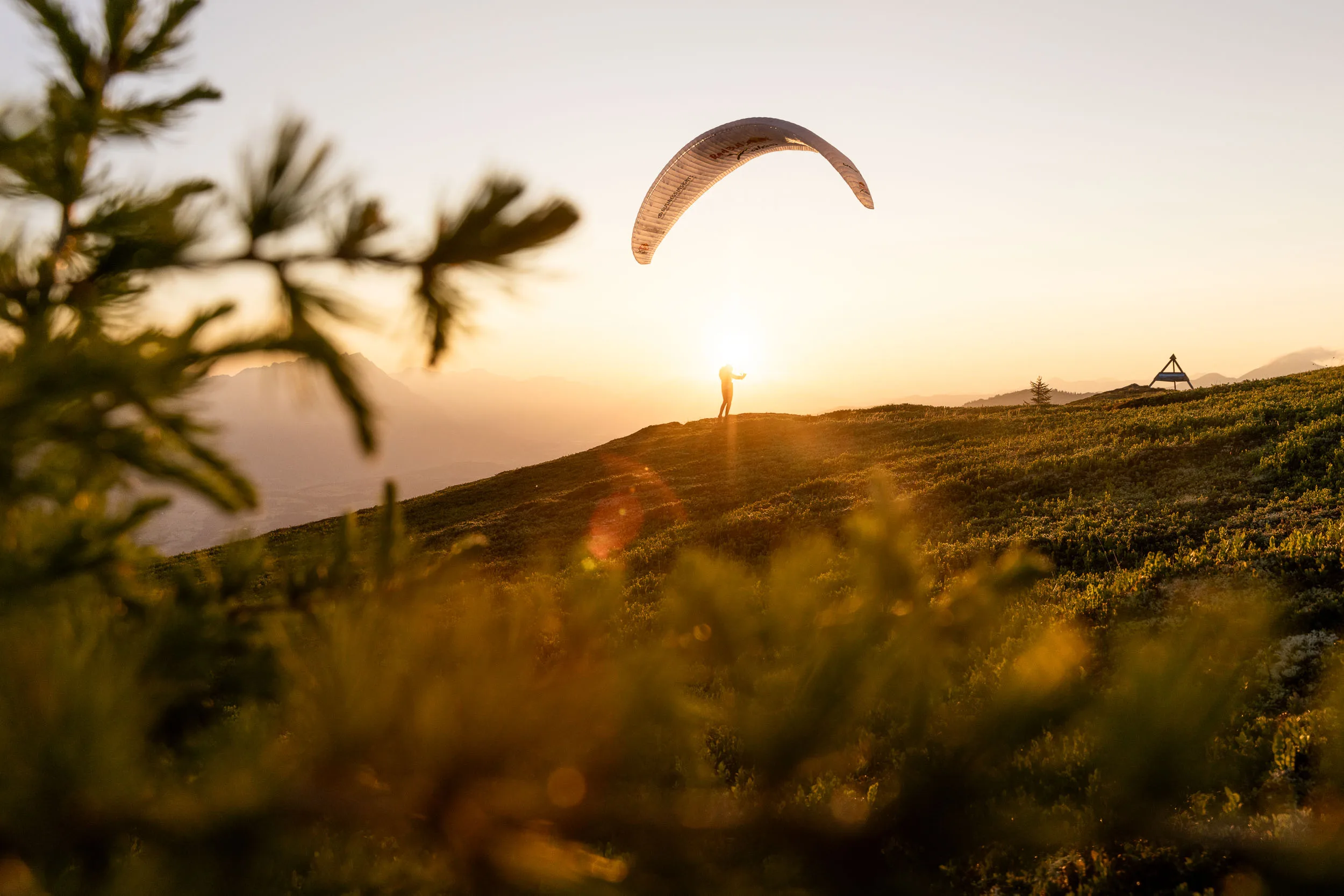 Gleitschirmpilotin startet unter ihrem Schirm vor der Morgensonne