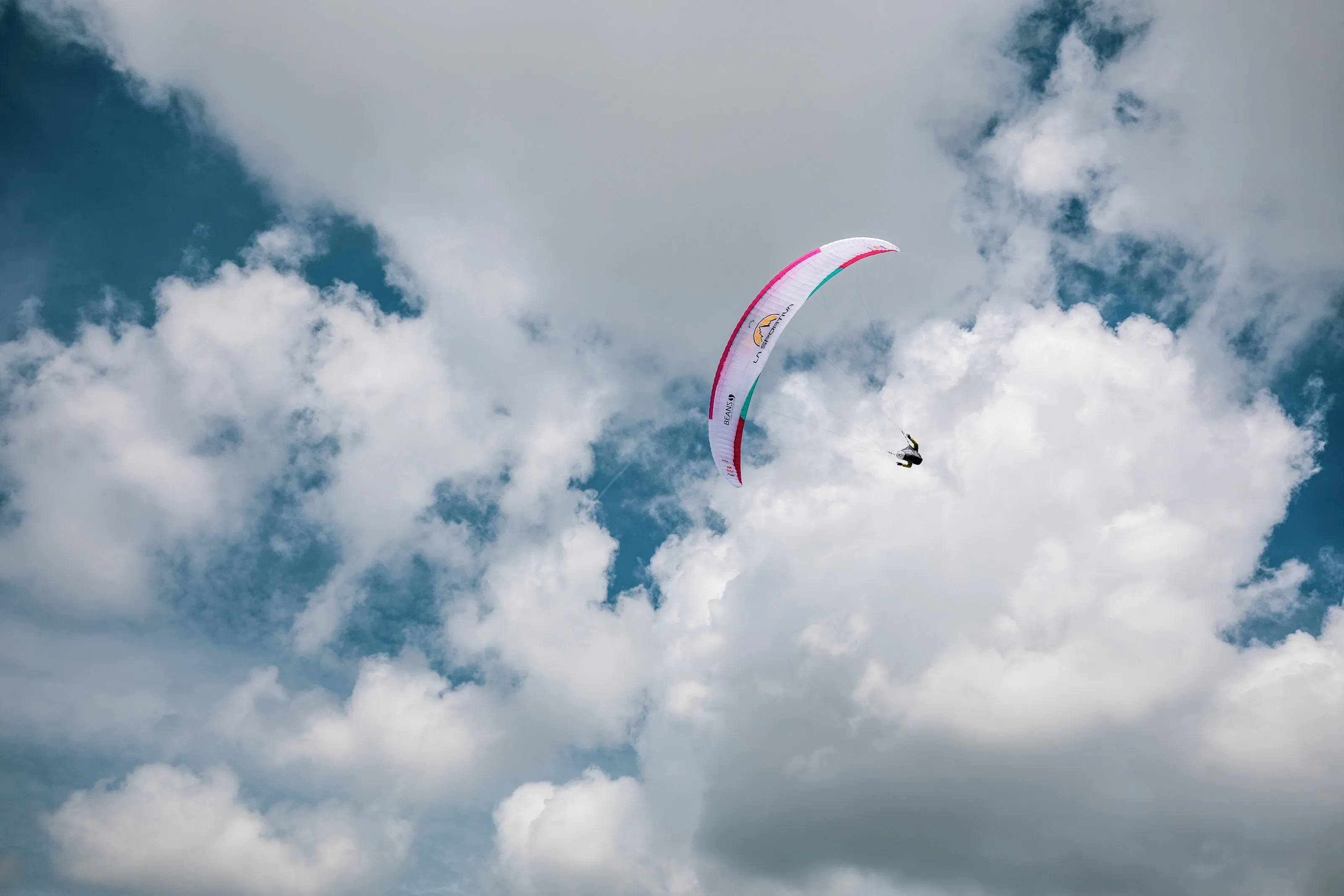 Michael Lacher fliegt unter dem pinkweißen Schirm vor aufgelockerten Wolken.