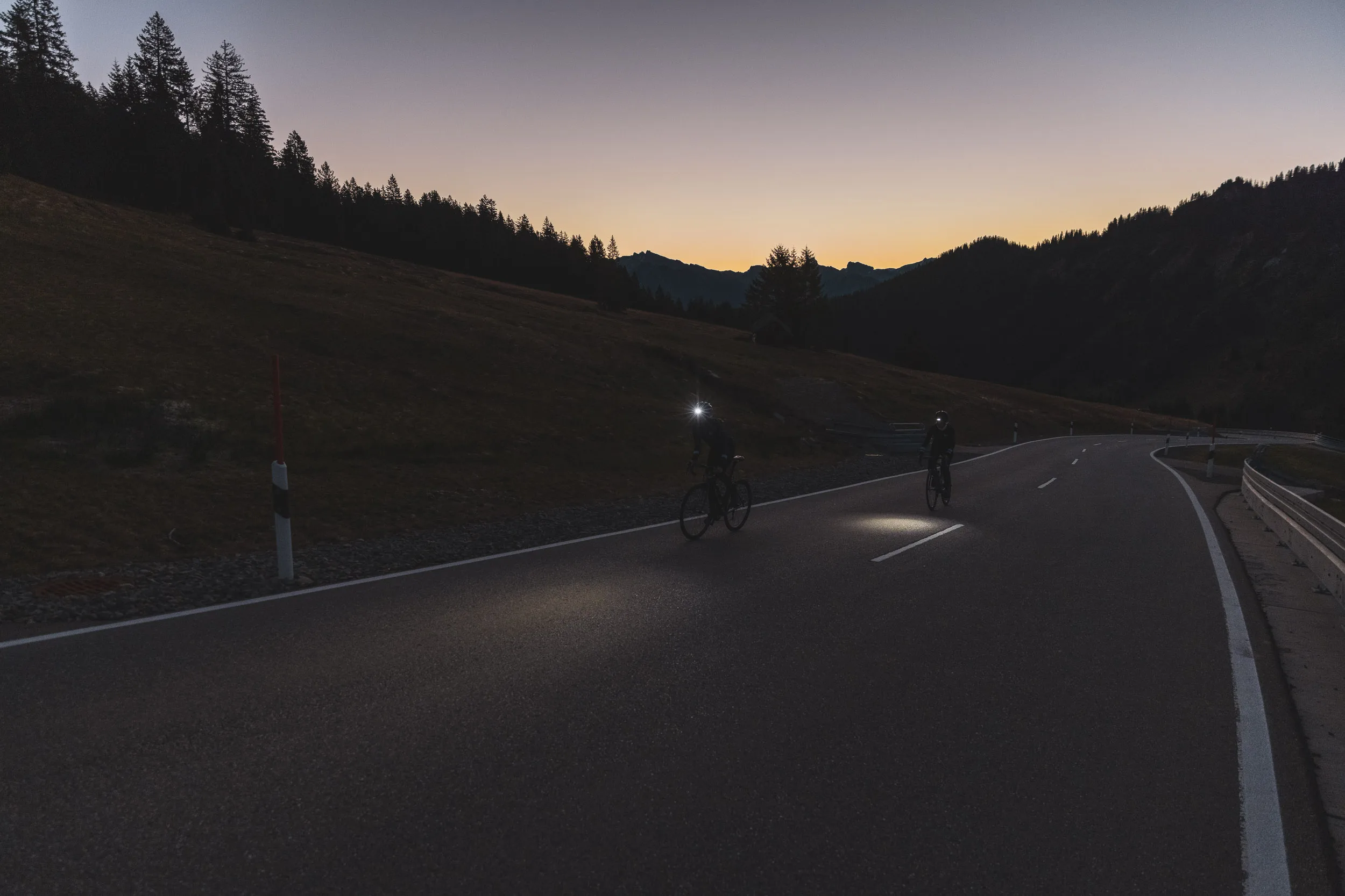 Zwei Rennradfahrerinnen auf einer Passstraße kurz vor Sonnenuntergang