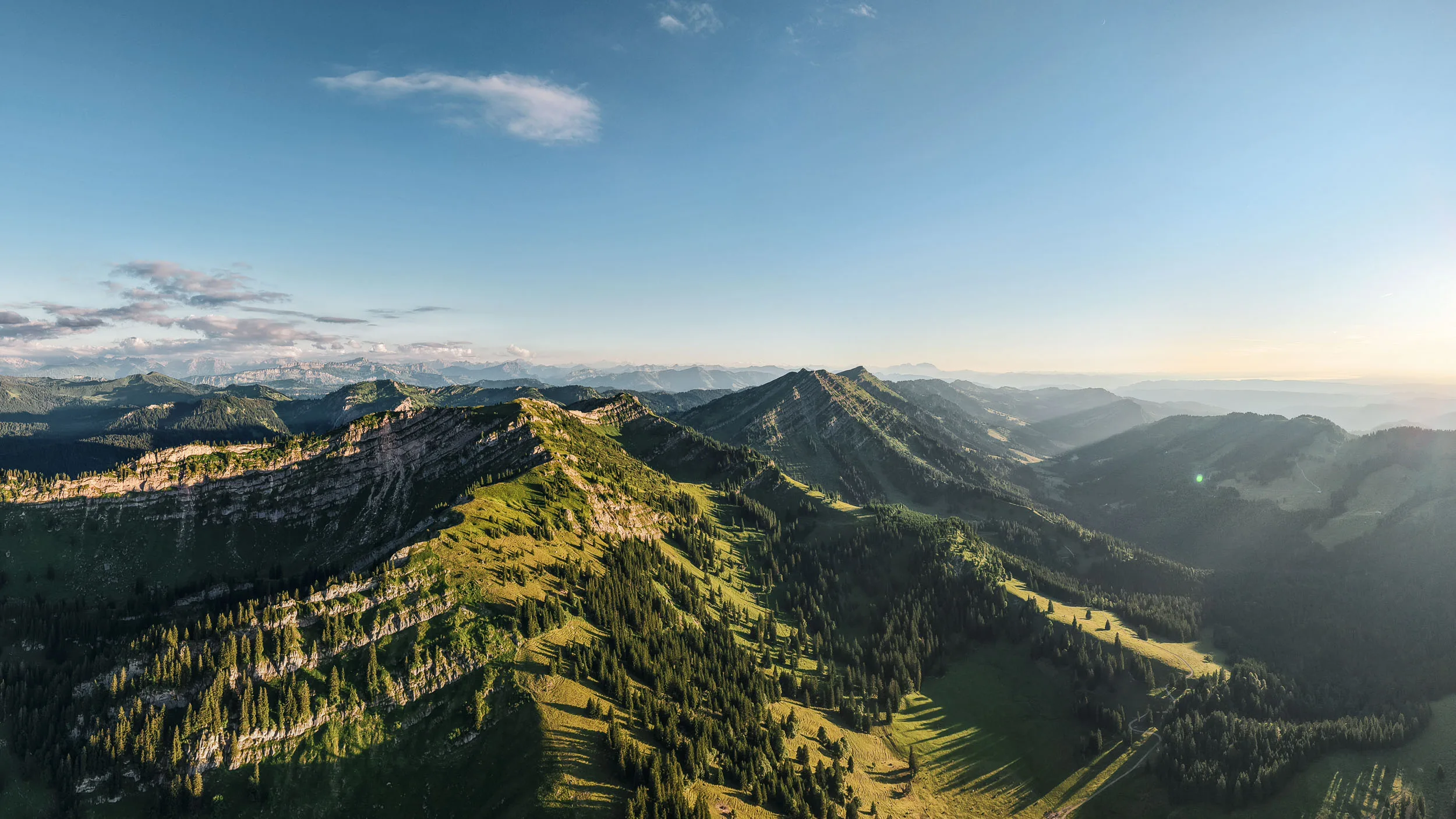 Luftaufnahme der Nagelfluhkette mit sonnigen Hängen, dunklen Tälern und weitem blauem Himmel.