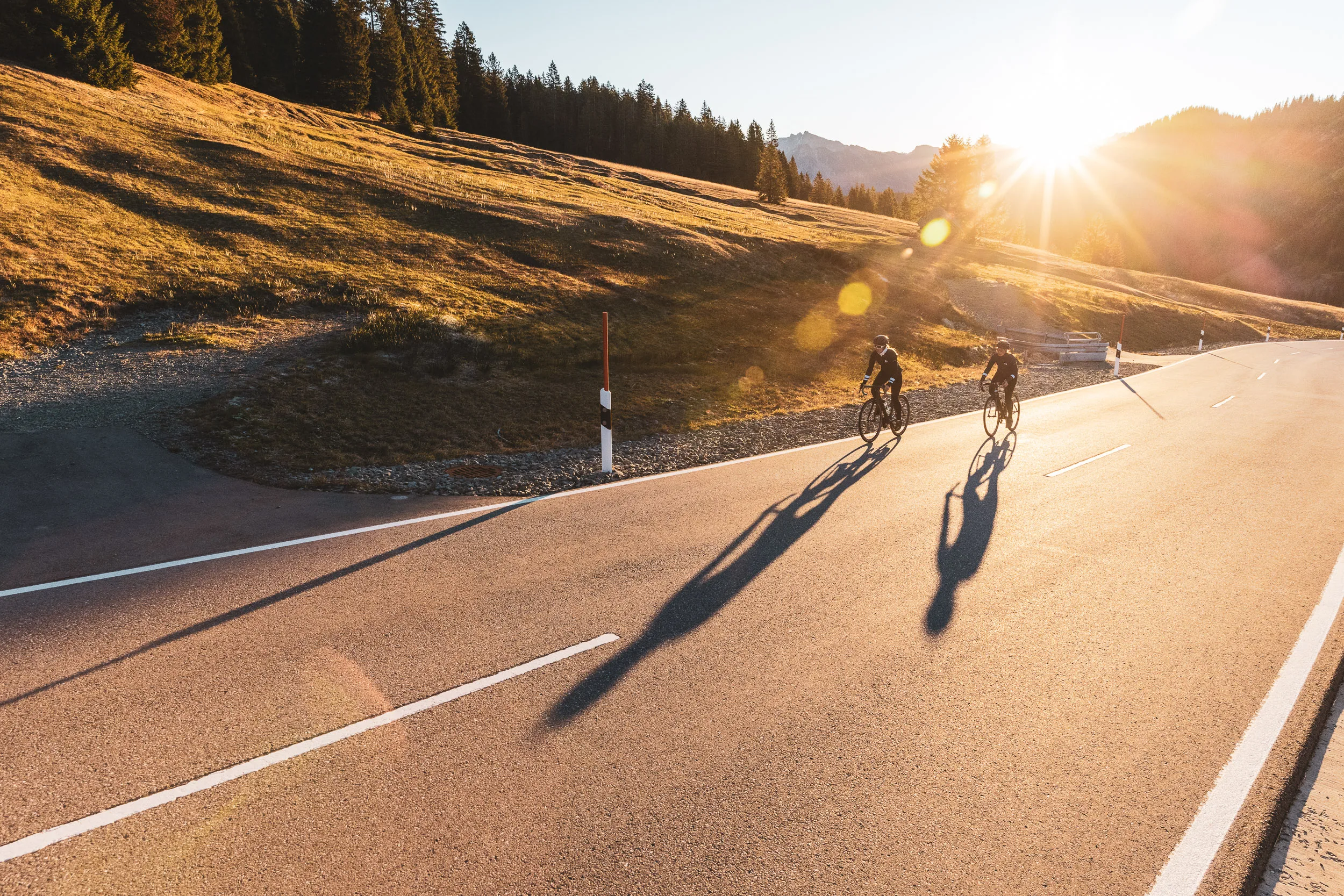Luftaufnahme von zwei Rennradfahrerinnen mit langen Schatten auf der Passstraße