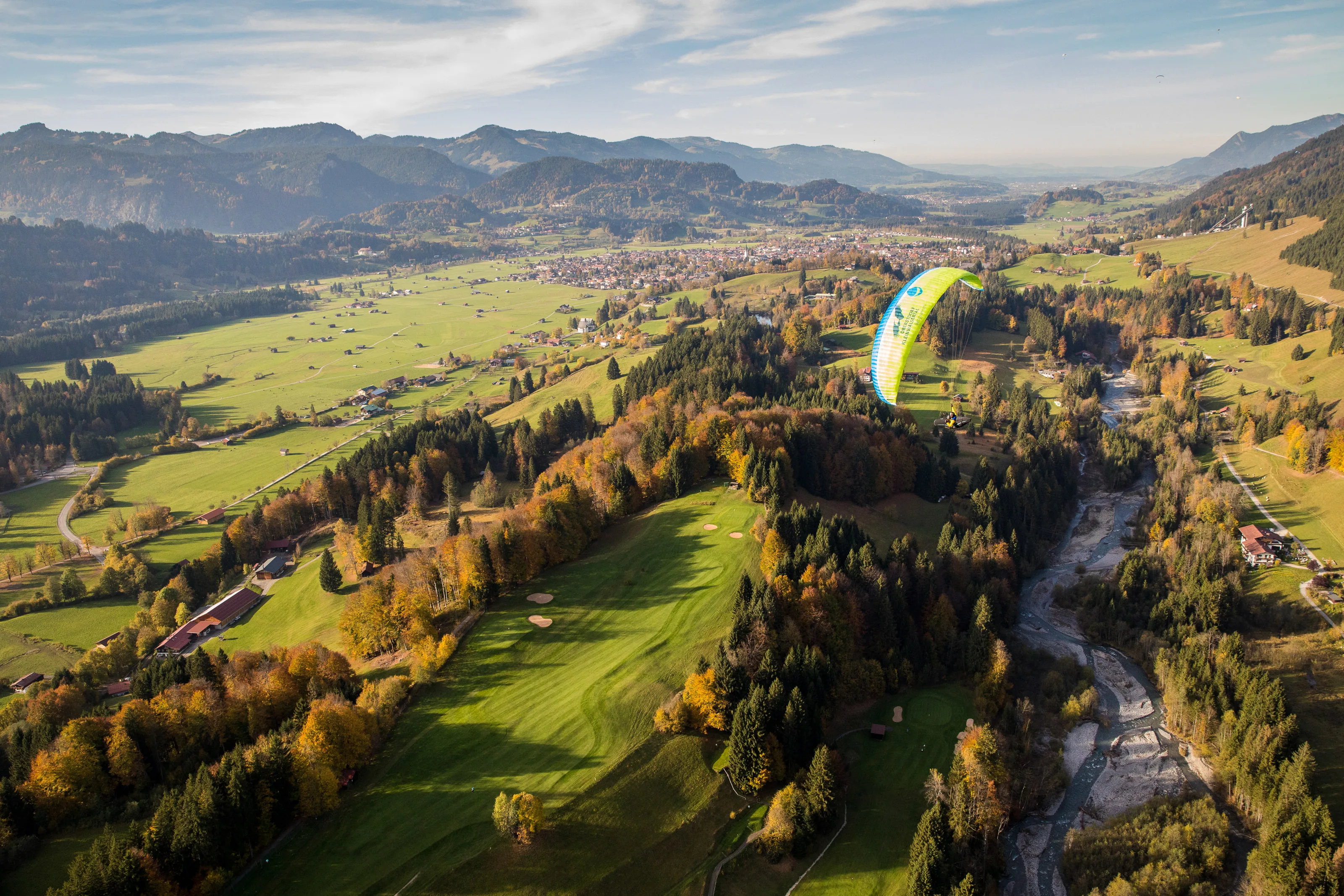 Michael Gebert schwebt mit grünem Gleitschirm über dem Oberstdorfer Tal vor einer weiten herbstlichen Bergkulisse
