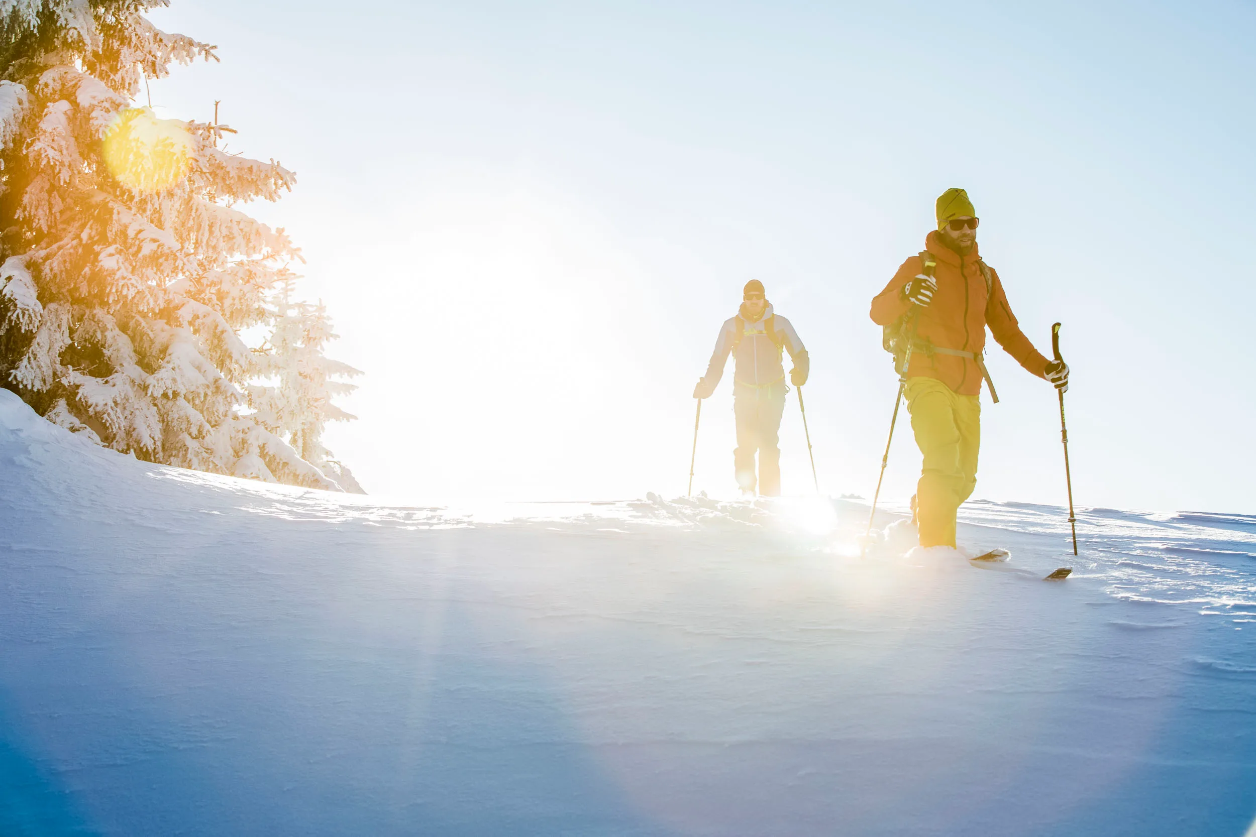 Zwei Skitourengeher steigen mit Fellen in der tiefen Wintersonne auf.