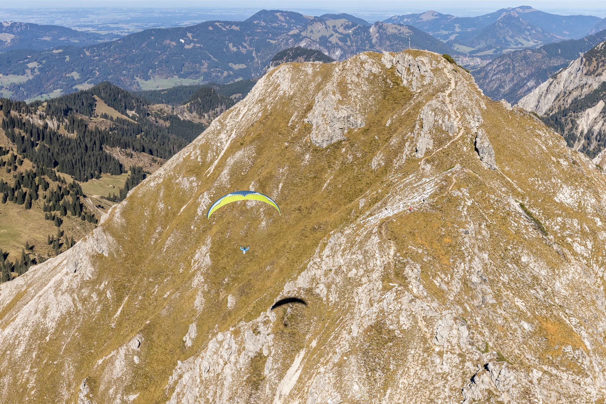 Michael Schnetzer gleitet mit dem Gleitschirm über einen herbstlichen Bergkamm bei Oberstdorf.