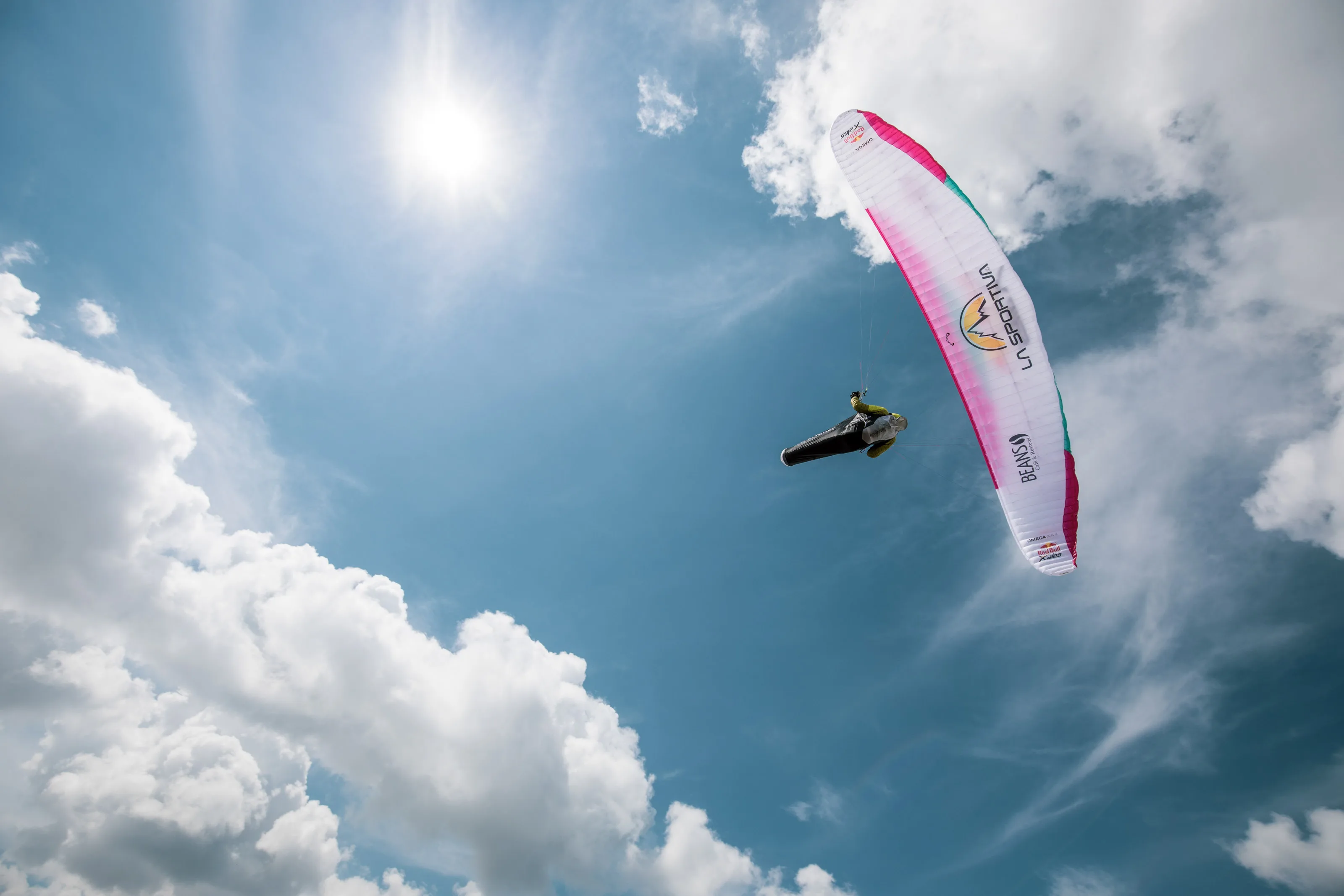 Von unten gesehen füllt der pinkweiße Gleitschirm den Himmel; Sonnenlicht bricht durch dünne Wolken.