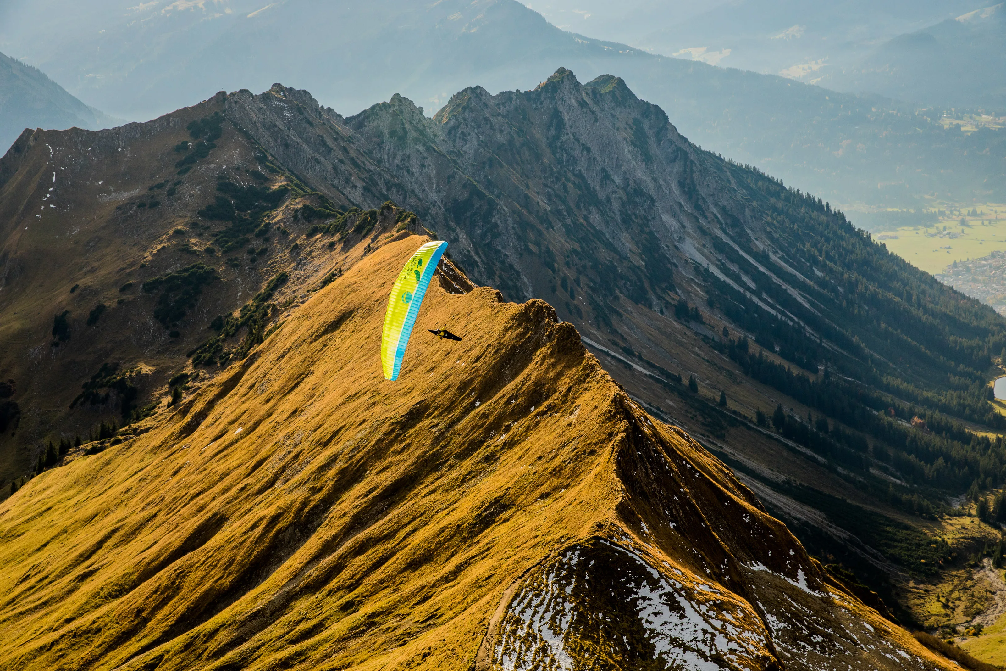 Michael Gebert schwebt mit grünem Gleitschirm über einem von Herbstgras geprägten Grat am Nebelhorn
