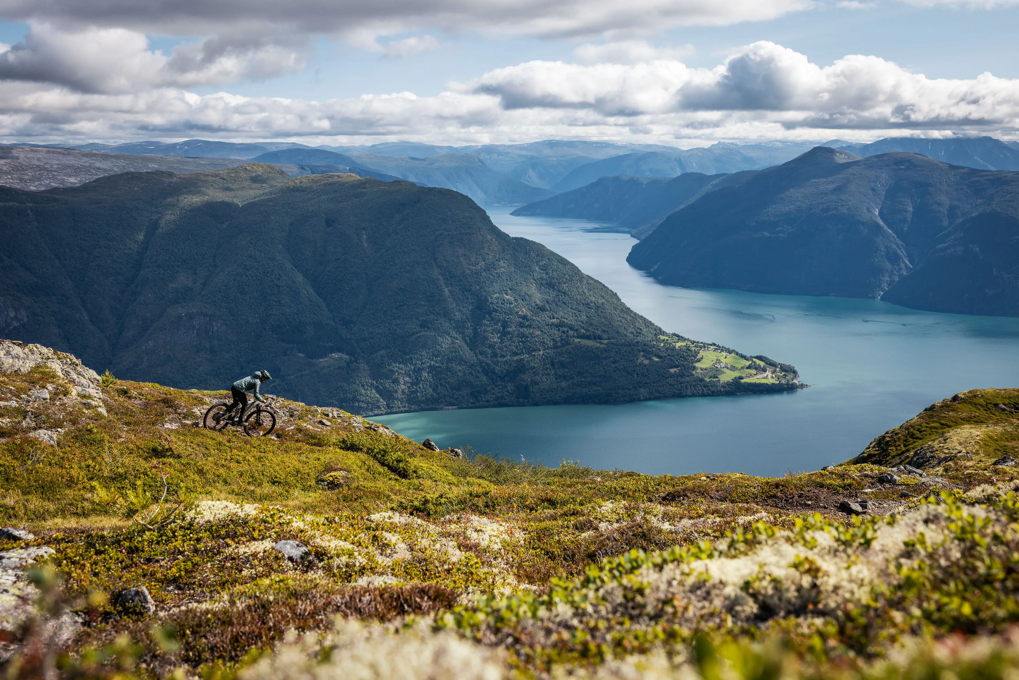 Mountainbiker fährt auf einem Höhenweg mit weitem Blick über den Fjord