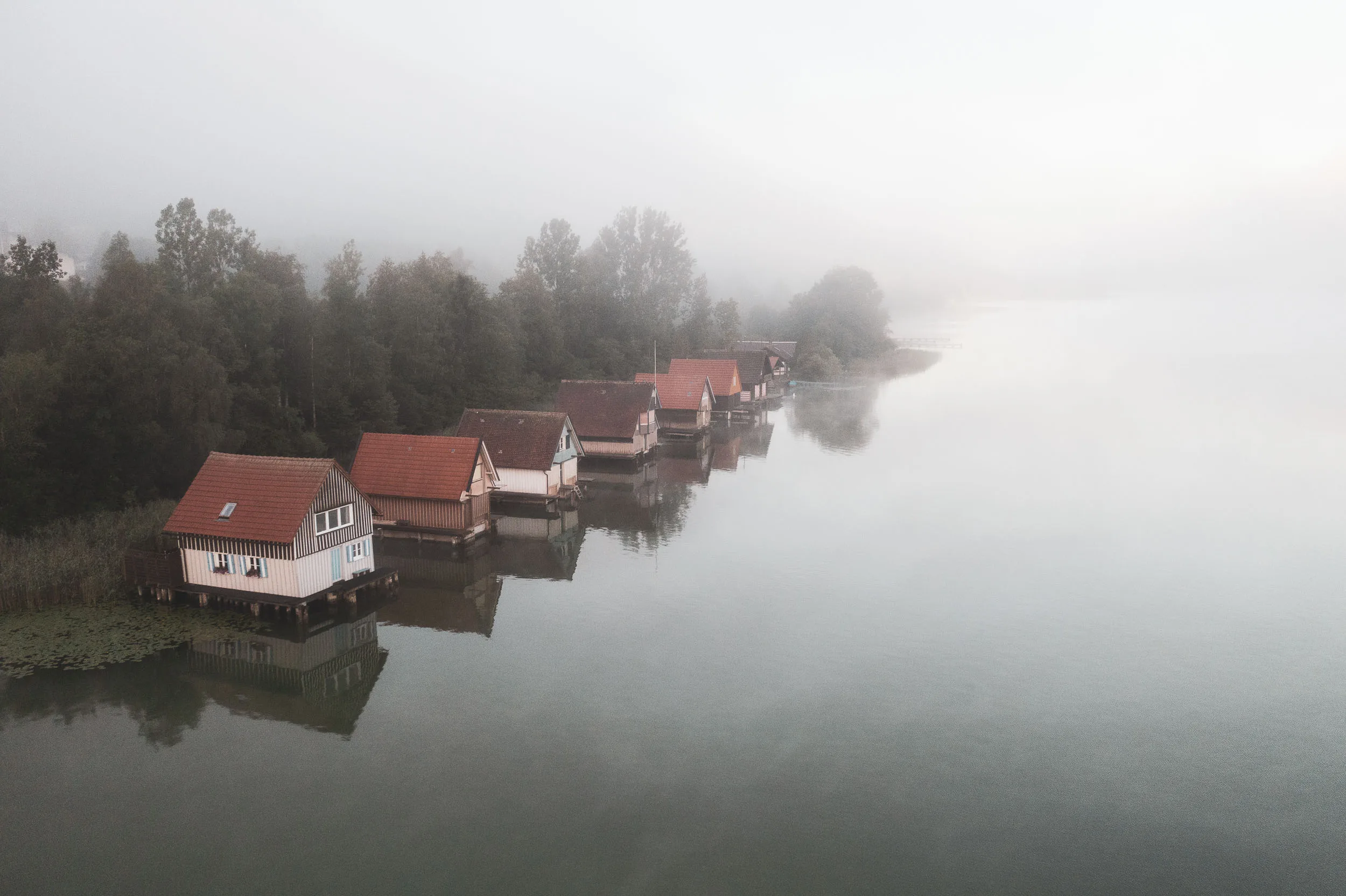 Luftaufnahme des Alpsees bei Immenstadt mit Uferhäusern und aufziehendem Morgennebel.
