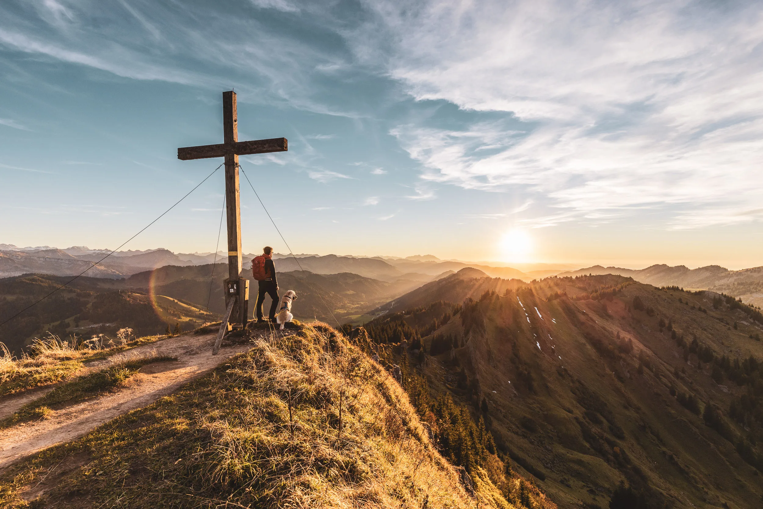 Andreas Kögel und Oskar stehen gemeinsam am Gipfelkreuz im goldenen Abendlicht