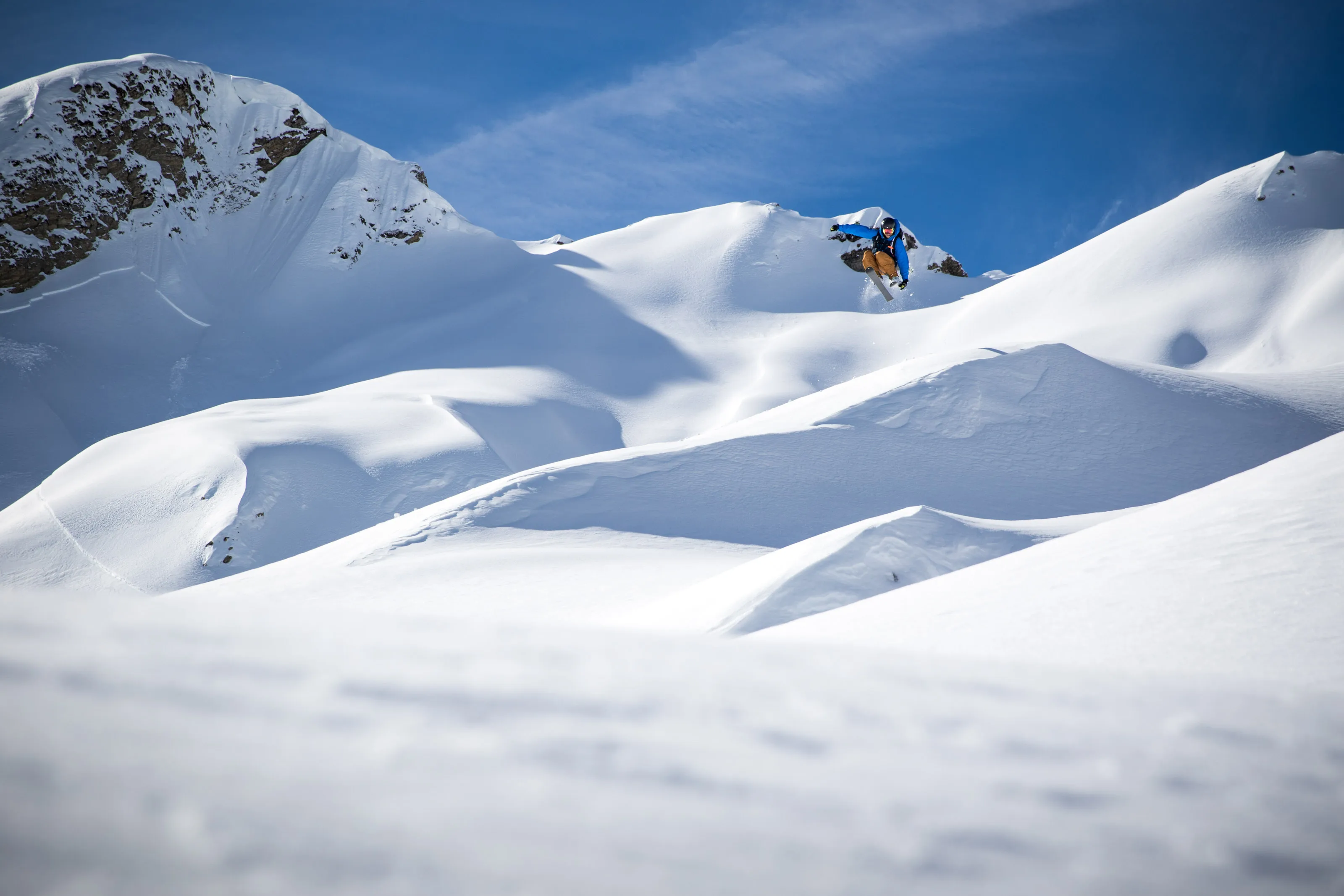 Skifahrer springt mit den Ski über eine Schneekante im Tiefschnee.