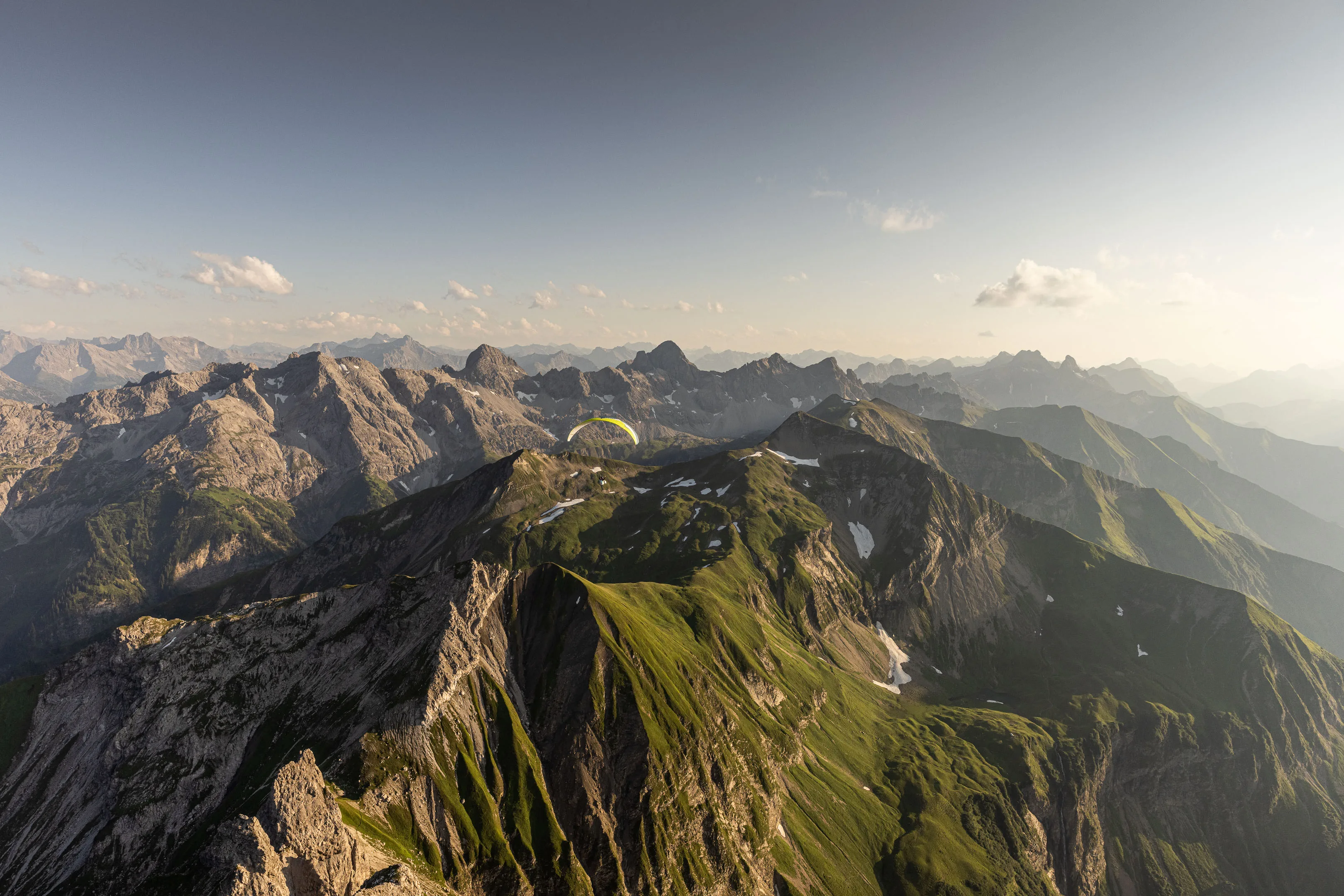 Ein Gleitschirm zieht fern über einen langen Grat mit Gipfeln bis zum Horizont