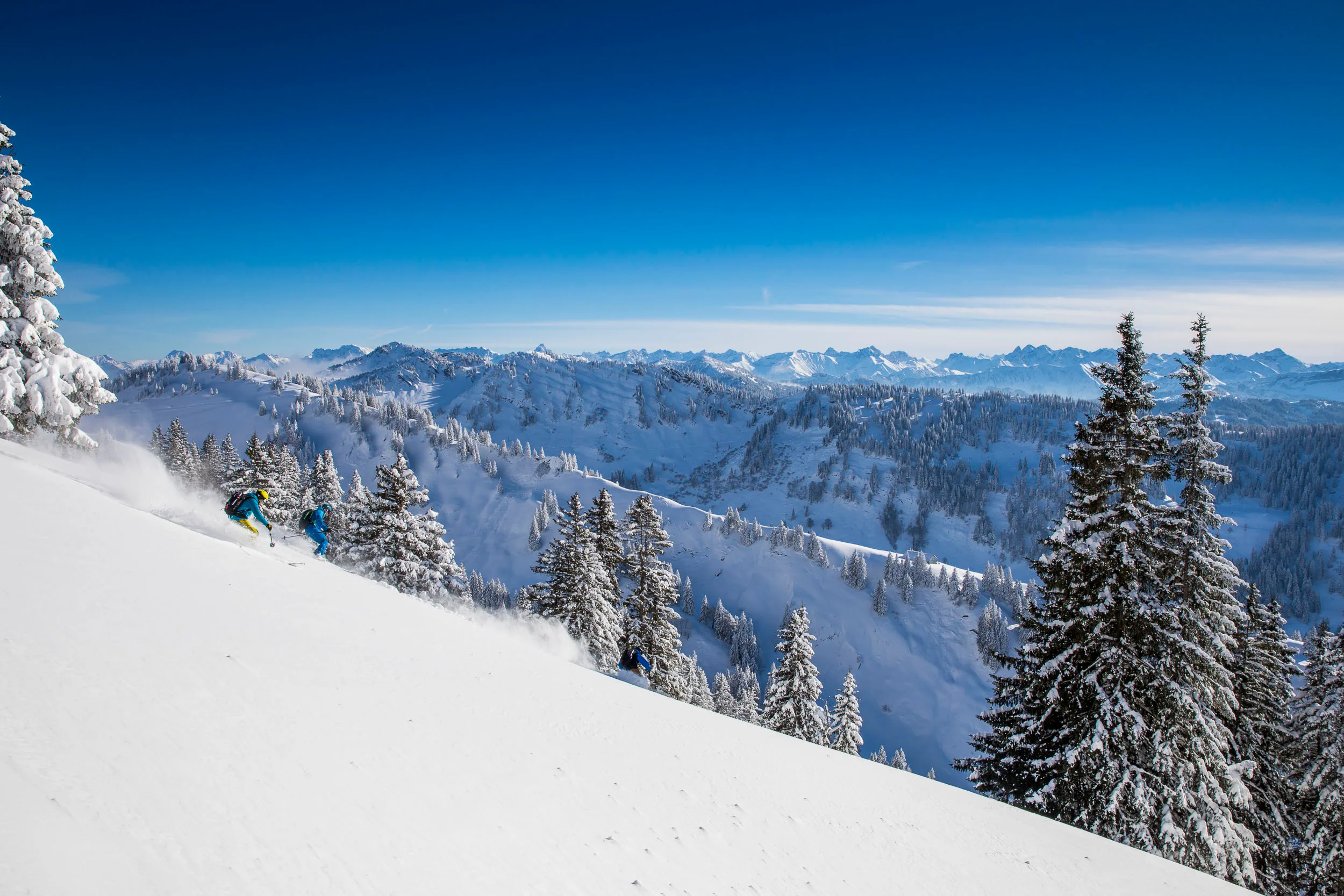 Skifahrerin fährt über einen offenen Hang mit Blick auf verschneite Berge.