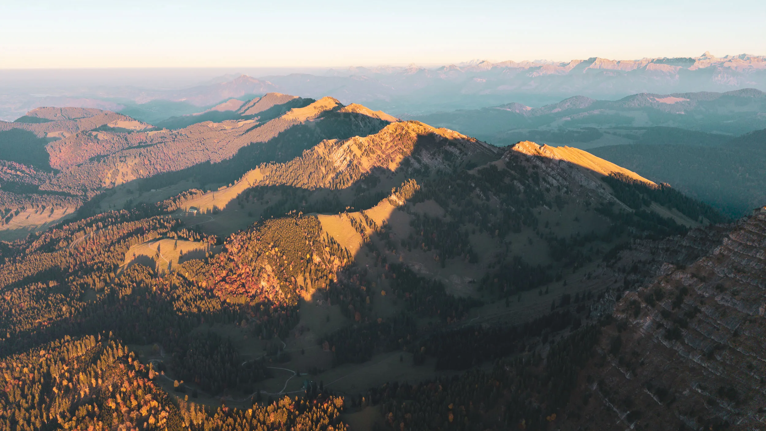 Luftaufnahme mehrerer herbstlicher Bergzüge im goldenen Abendlicht