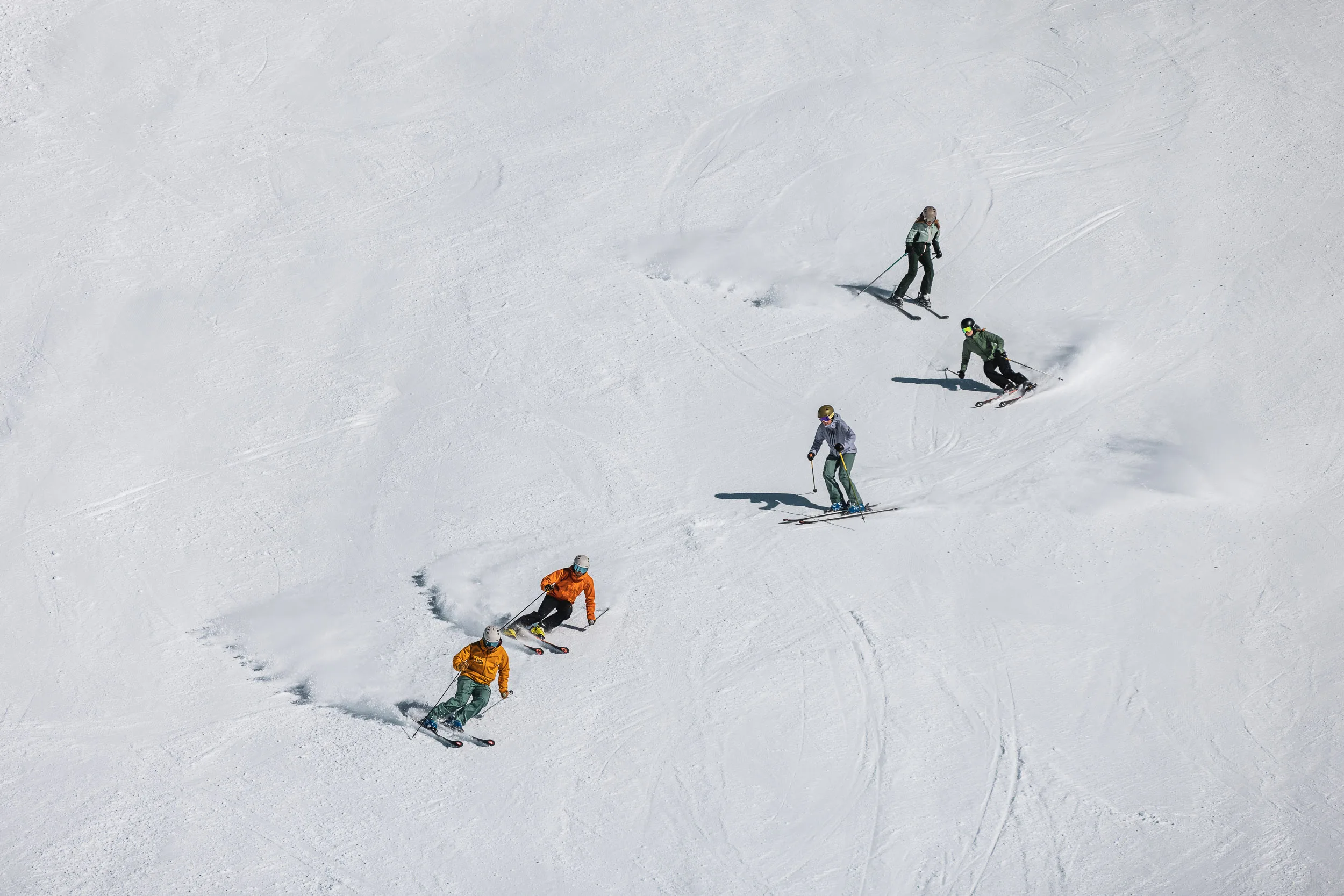 Vier Skifahrer ziehen versetzte Linien durch einen offenen Schneehang