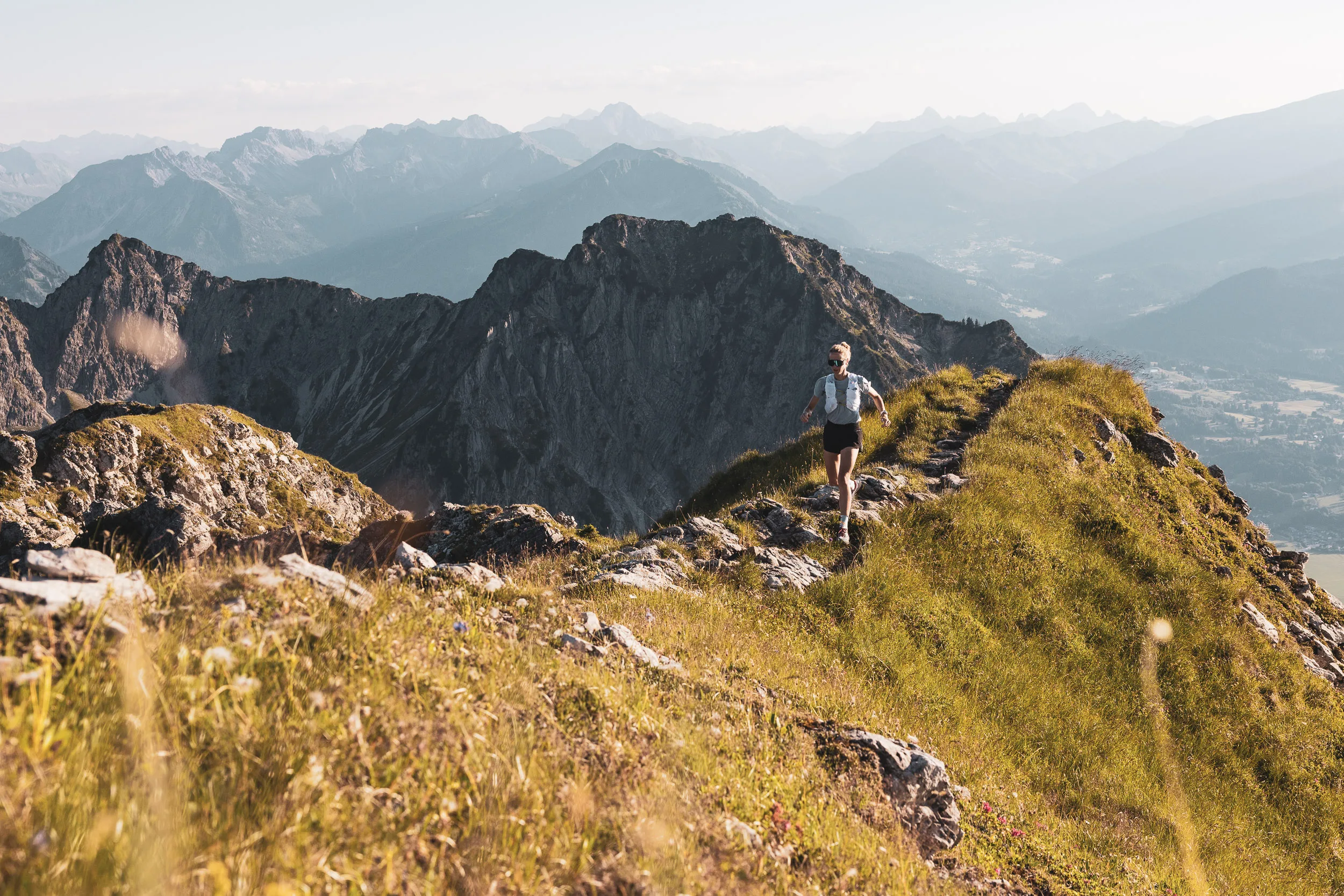 Trailrunnerin zwischen Gräsern auf einem Berggrat im warmen Abendlicht