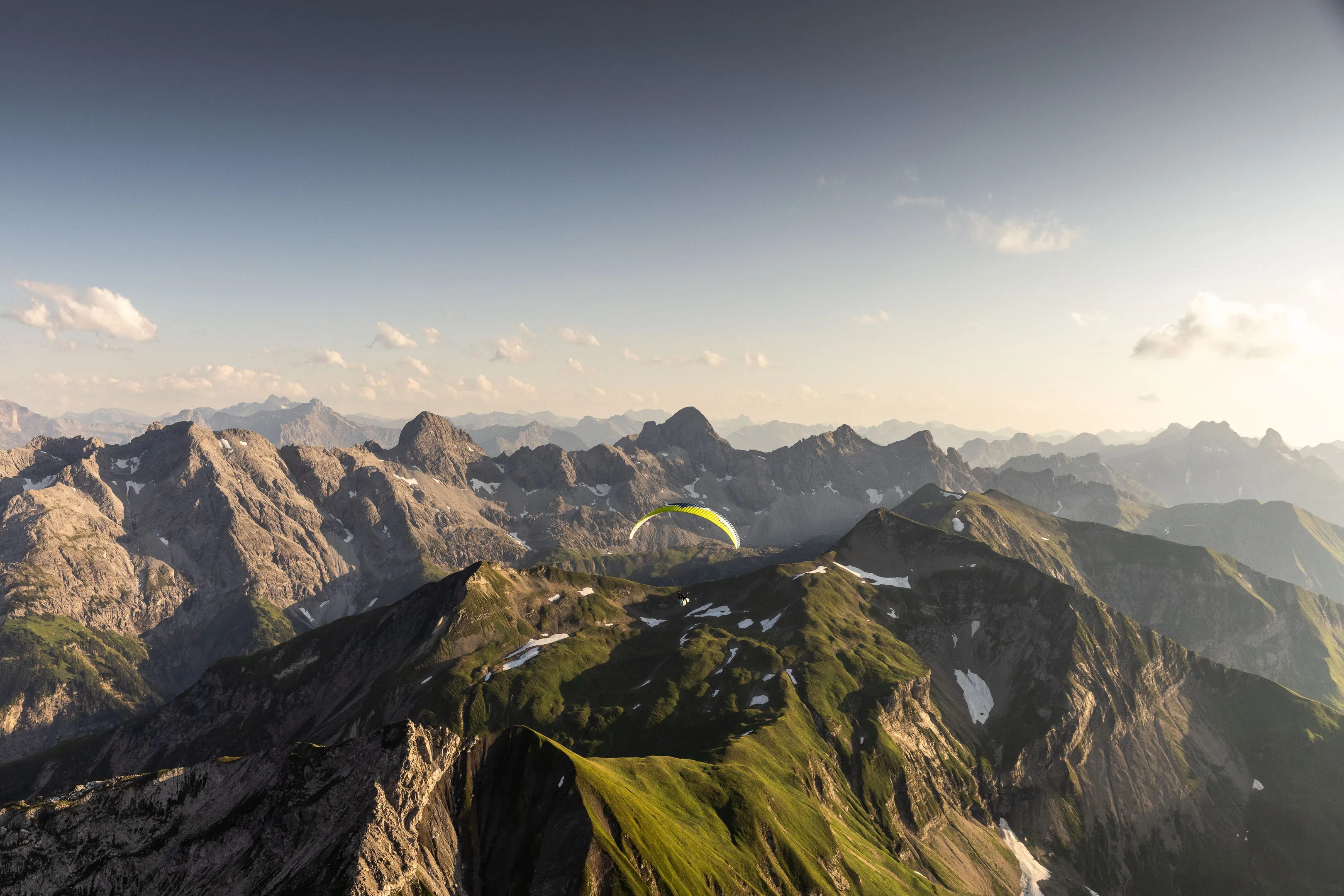 Ein kleiner Gleitschirm verschwindet fast in der Weite aus Graten und Abenddunst