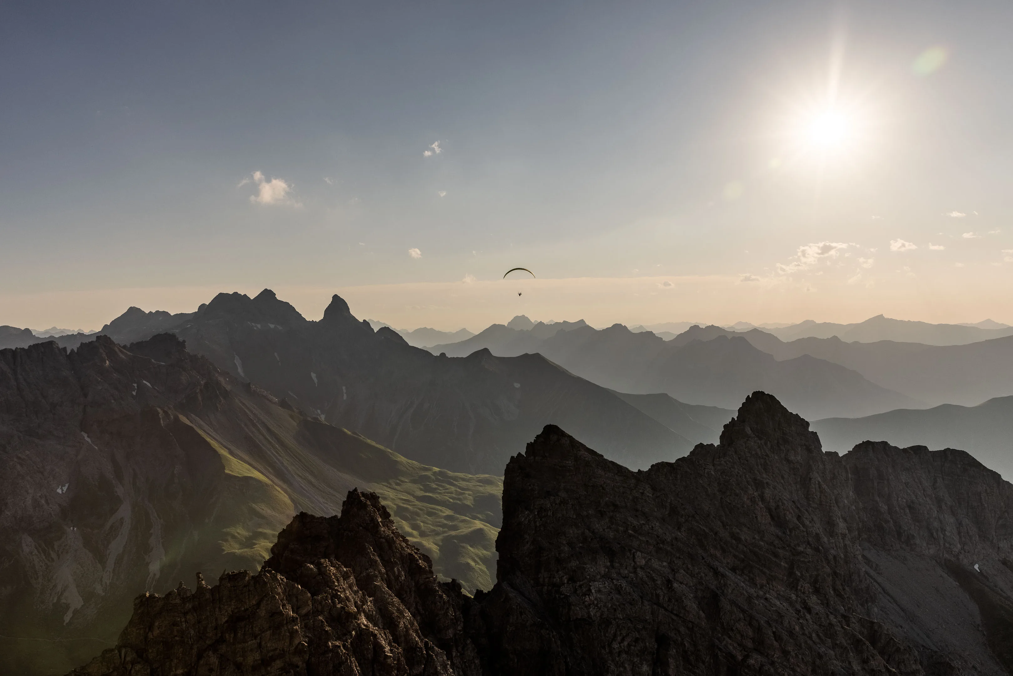 Ein kleiner Gleitschirm zieht unter der Abendsonne über gezackte Gipfelsilhouetten