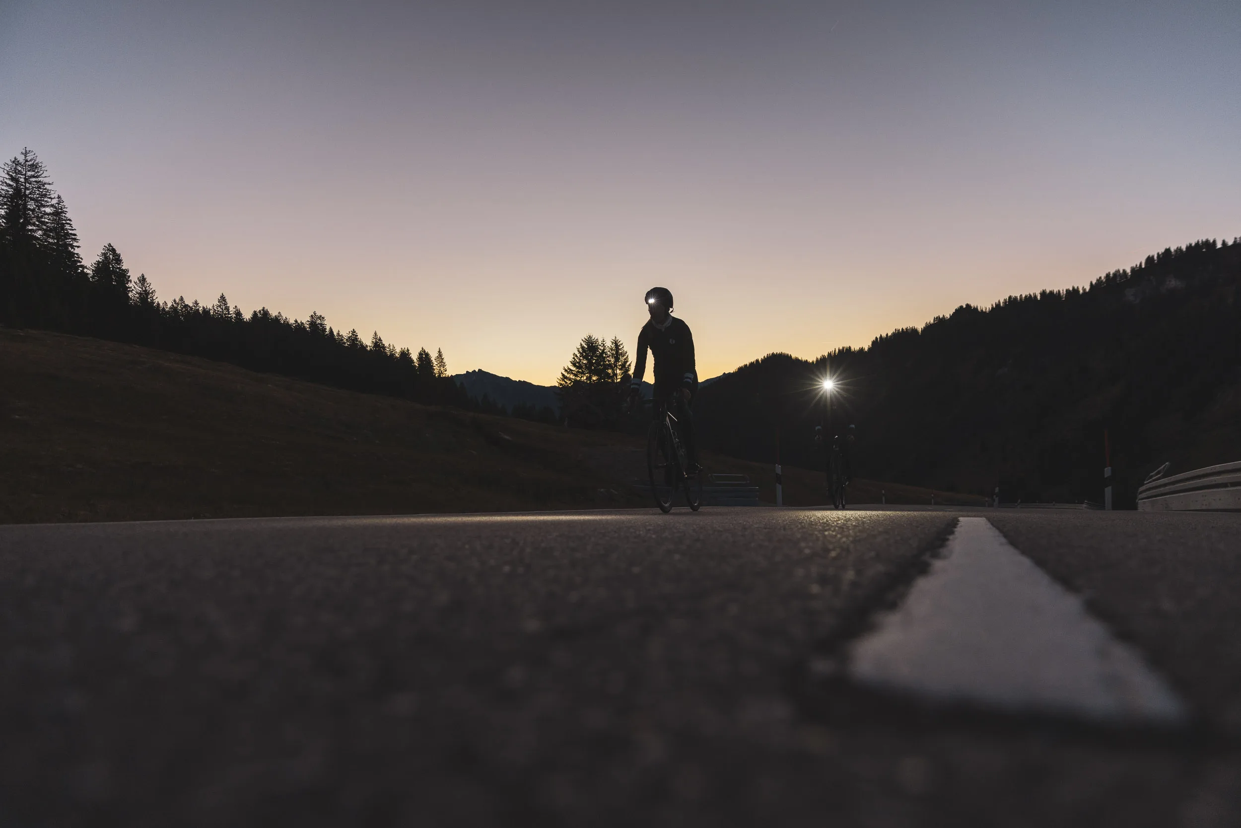 Rennradfahrerin als Silhouette auf der Passstraße im letzten Licht