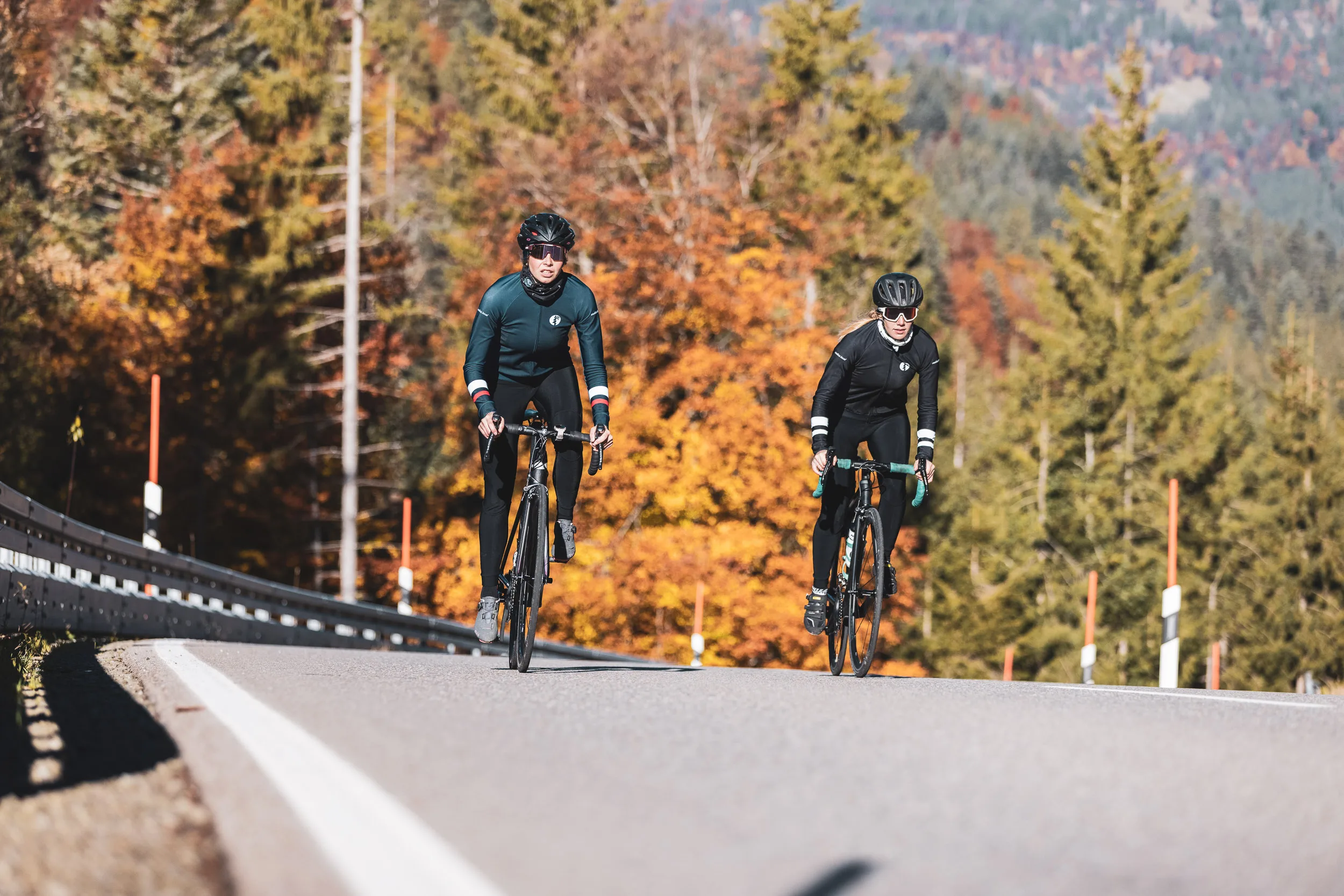 Zwei Rennradfahrerinnen fahren nebeneinander durch herbstliches Licht