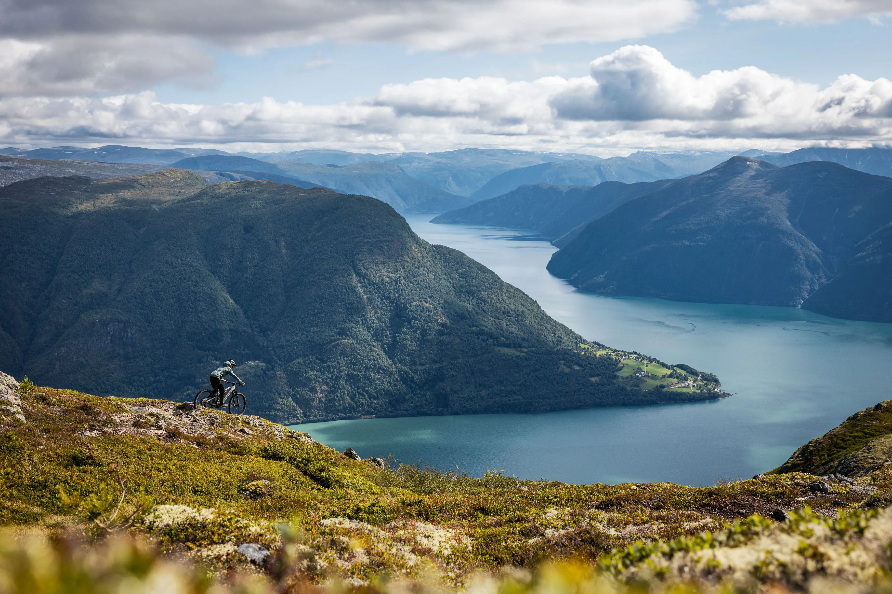 Mountainbiker folgt einem schmalen Trail hoch über einer Fjordlandschaft