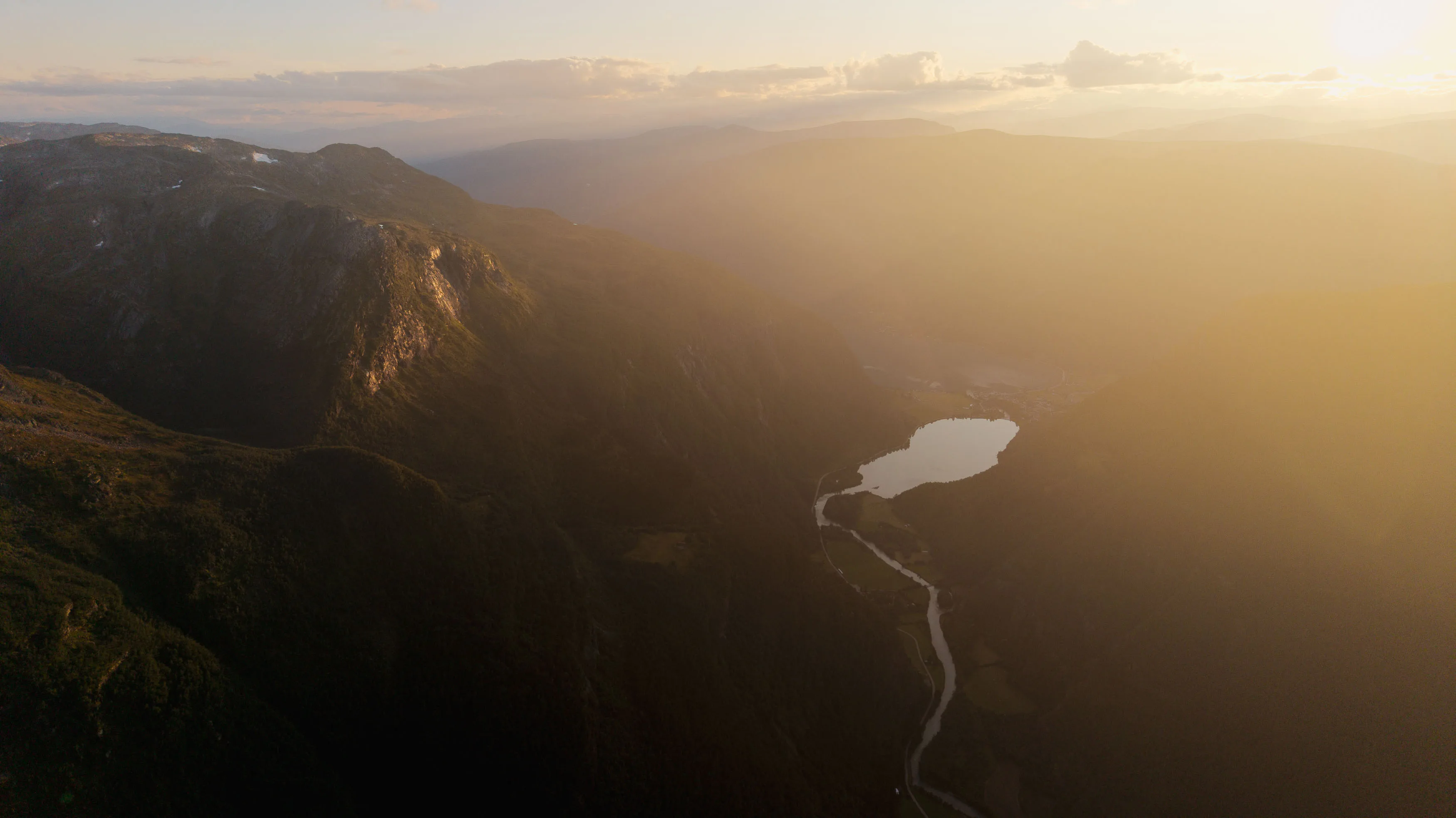 Goldenes Gegenlicht liegt über einem tiefen Bergtal mit See und gewundenem Fluss