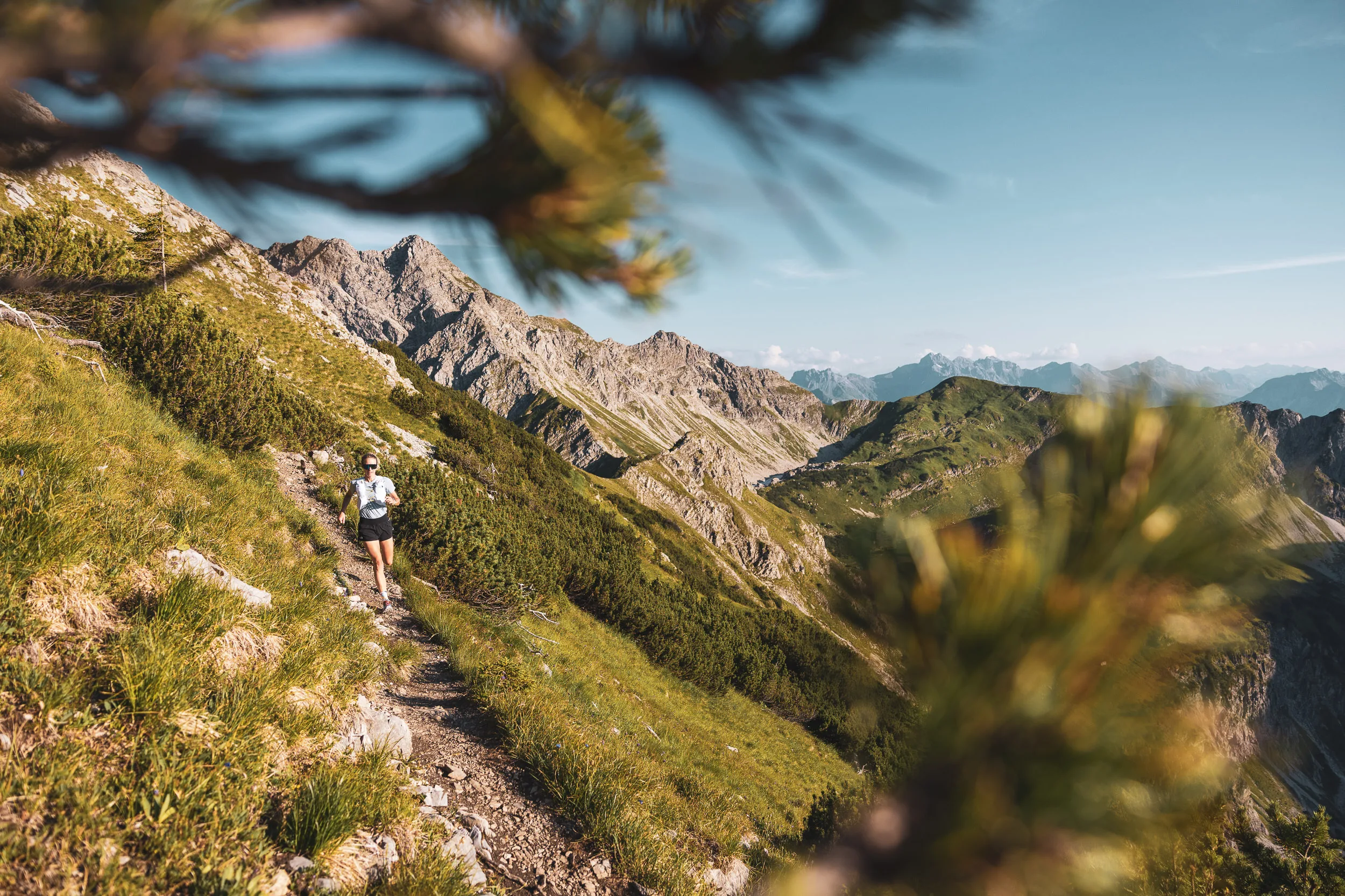 Trailrunnerin auf einem Bergpfad zwischen Latschen und felsigen Gipfeln