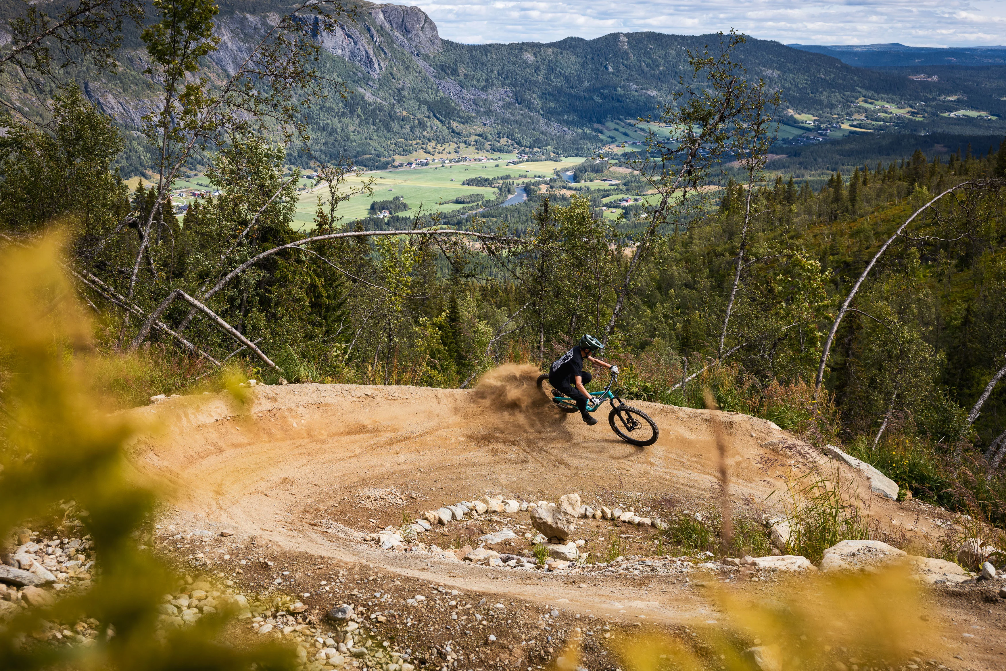 Mountainbiker zieht in einem staubigen Anlieger eine enge Linie über dem grünen Tal