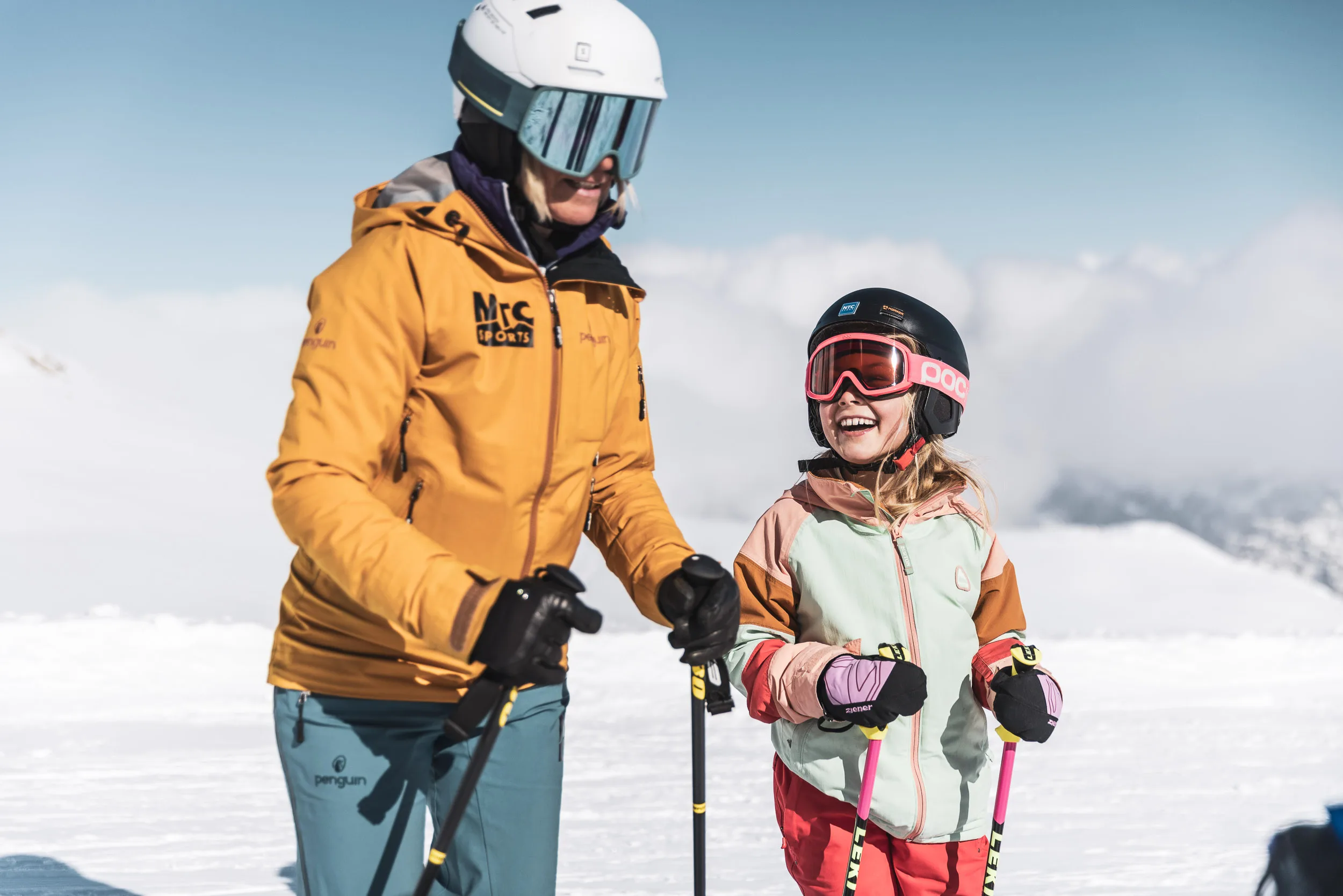 Skilehrerin steht mit einem lachenden Kind vor verschneitem Bergpanorama