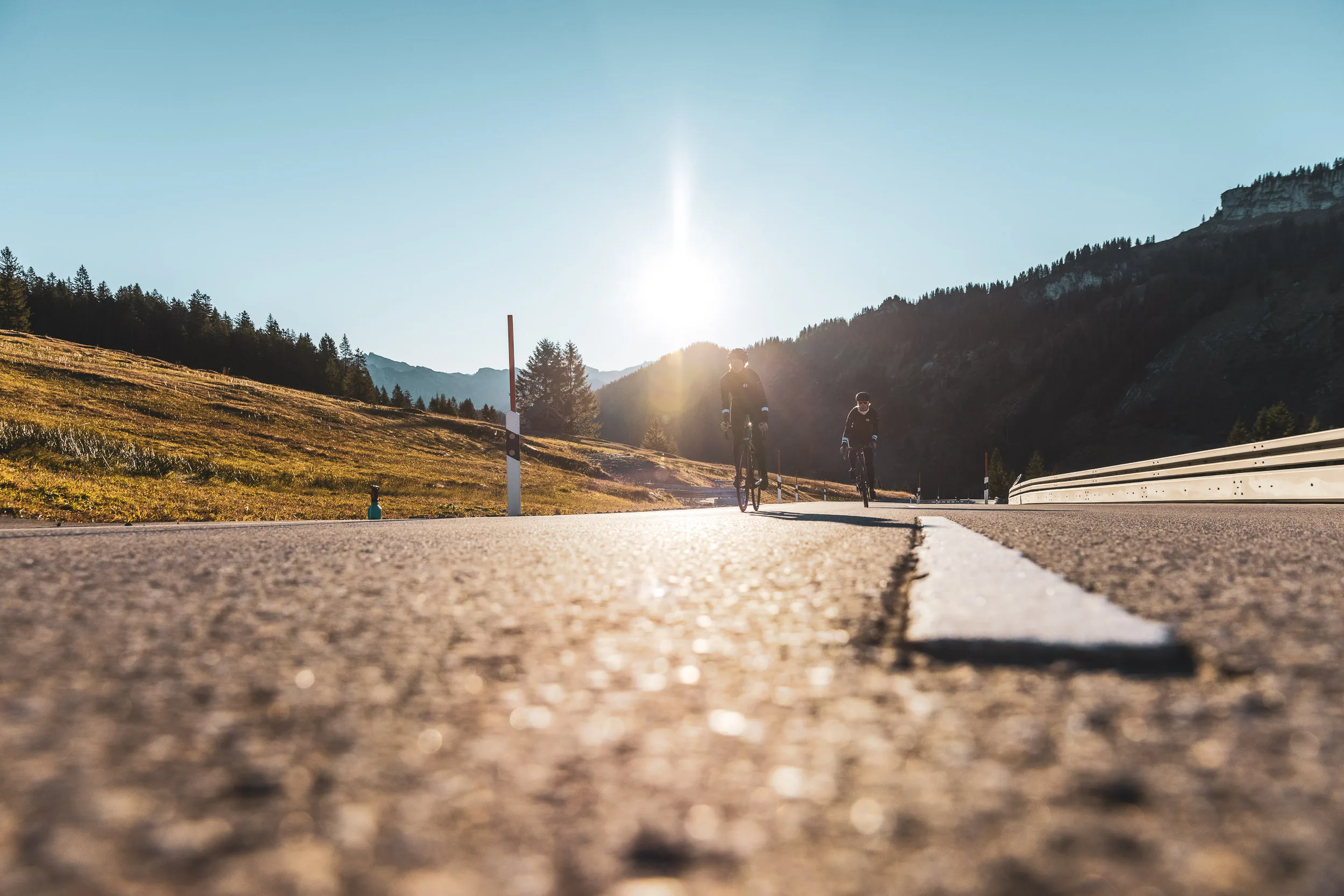 Zwei Rennradfahrerinnen fahren aus der Tiefe der Passstraße ins Licht