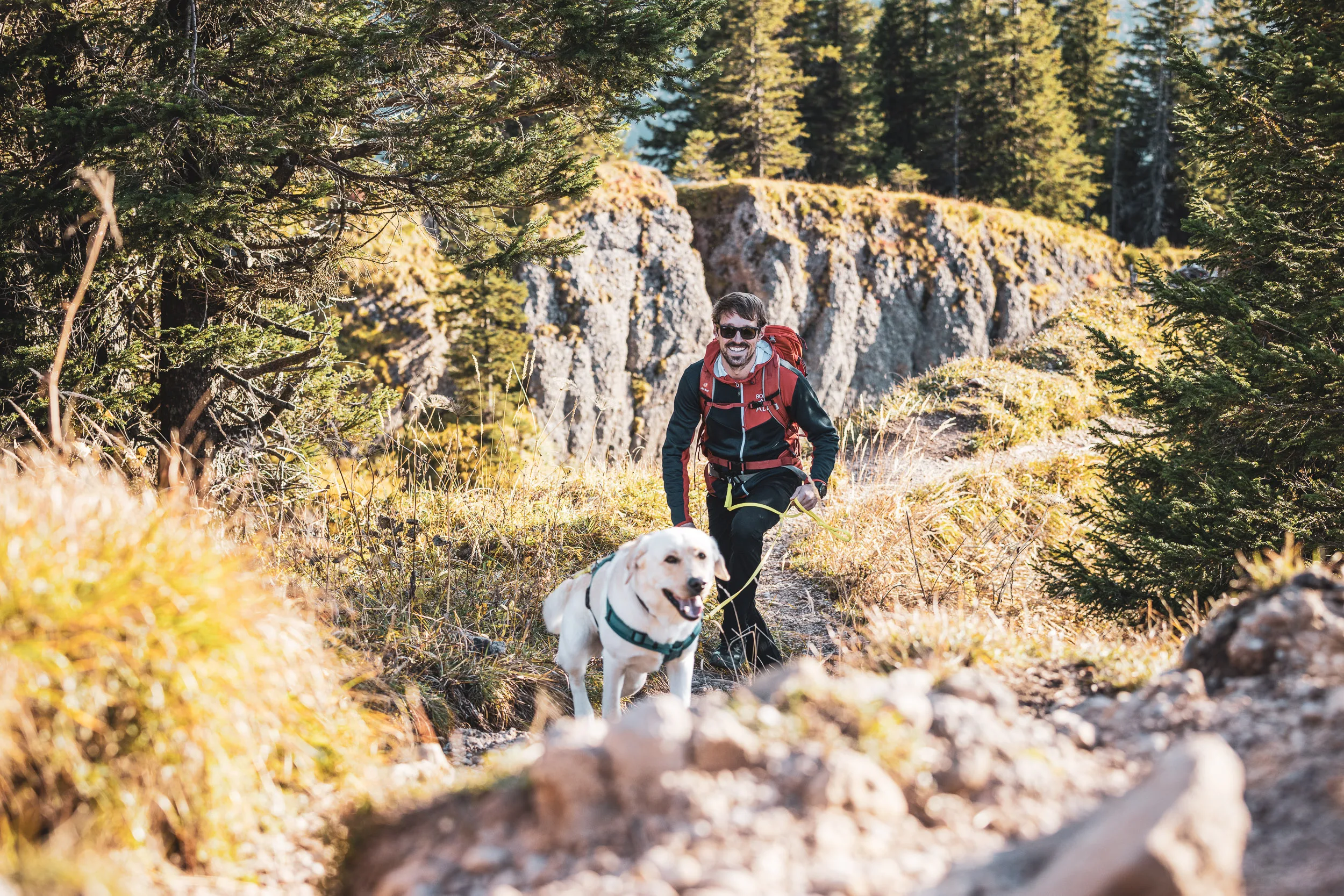 Andreas Kögel und Hund Oskar steigen über einen felsigen Bergpfad im Abendlicht auf