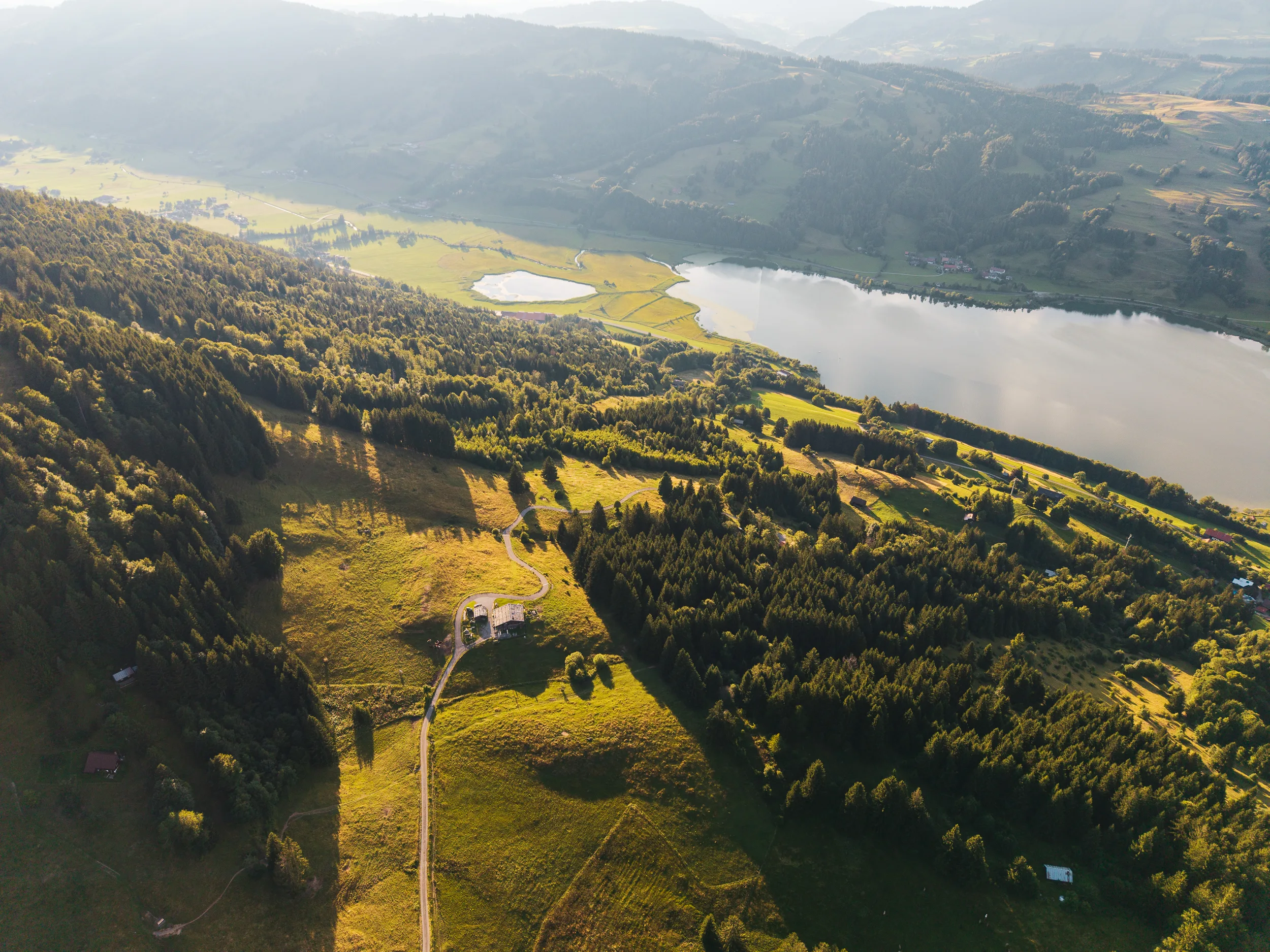 Weiter Luftblick vom Gschwenderberg über den Großen Alpsee im Abendlicht