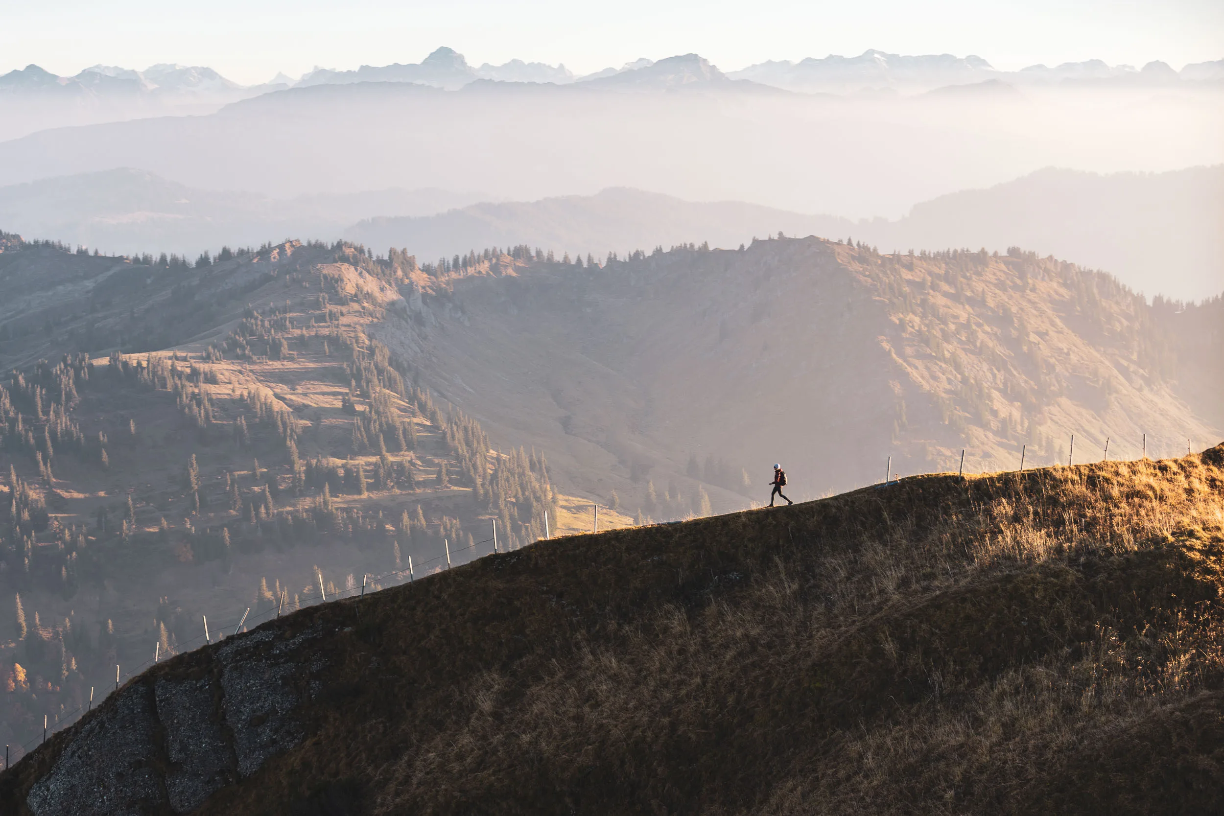 Wanderin bewegt sich als kleine Figur über einen dunklen Kamm vor fernen Gipfeln