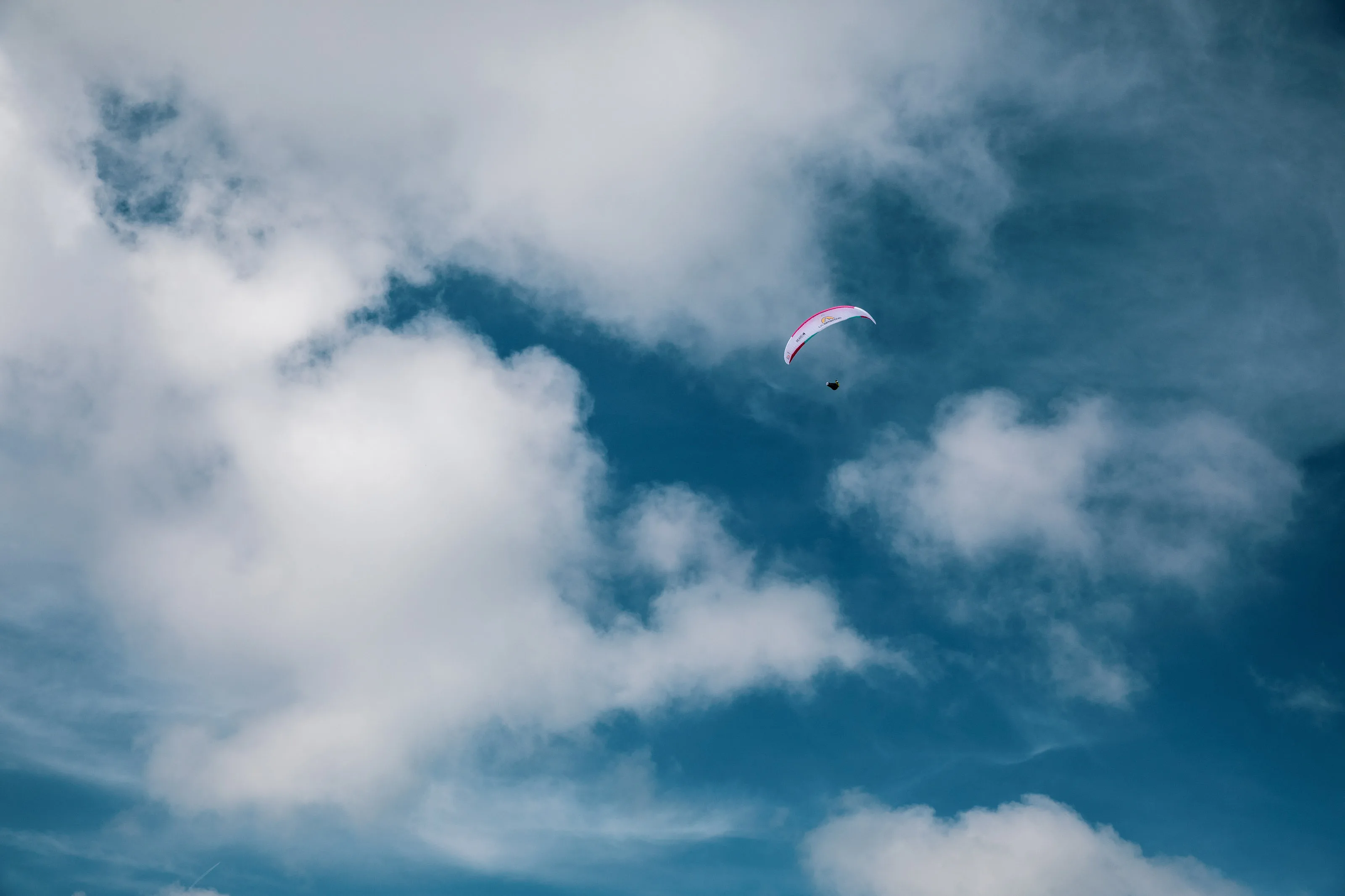 Michael Lacher fliegt unter einem kleinen pinkweißen Gleitschirm vor einer hohen Wolkenwand.