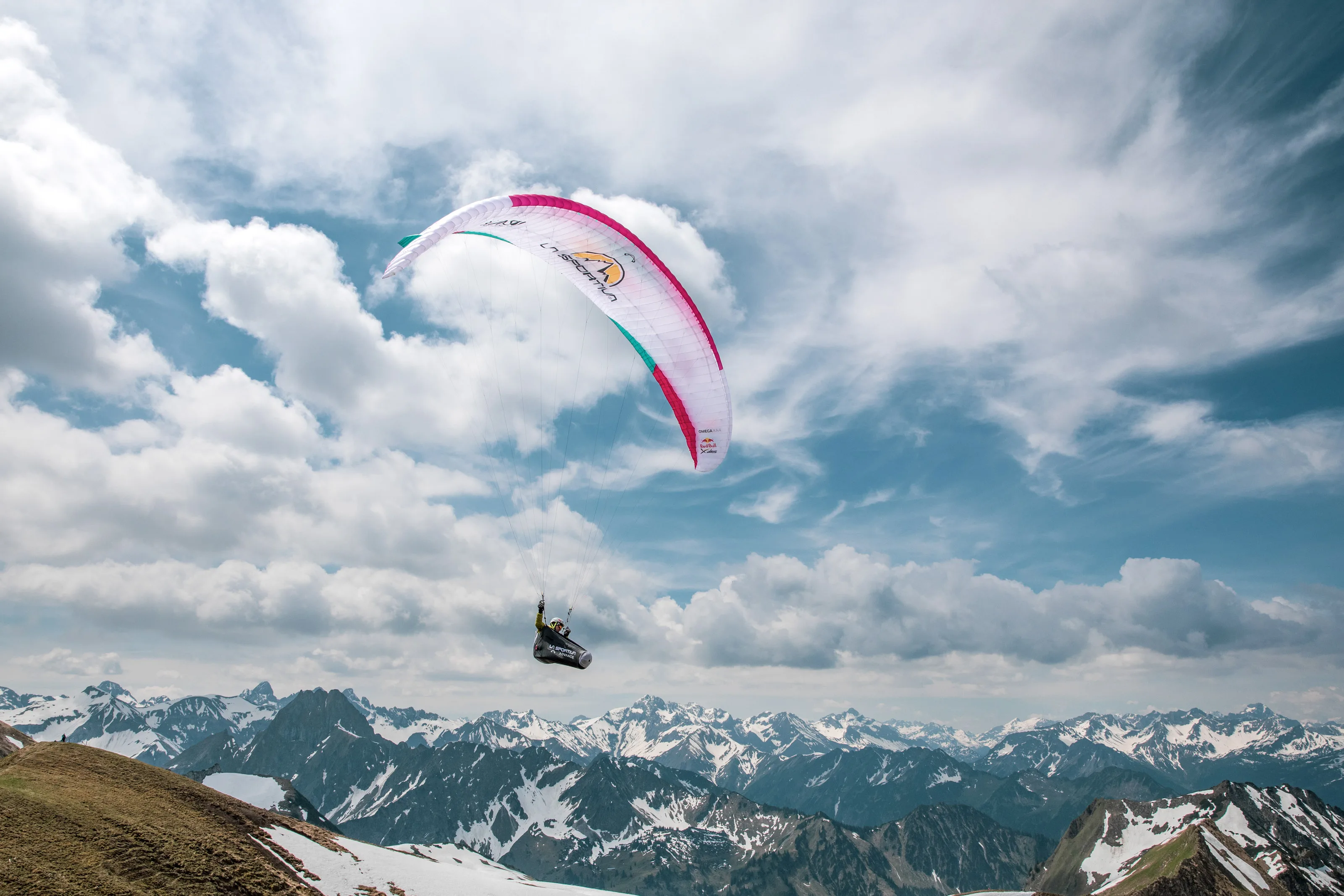 Der pinkweiße Gleitschirm von Michael Lacher schwebt vor hoch aufragenden Sommerwolken.