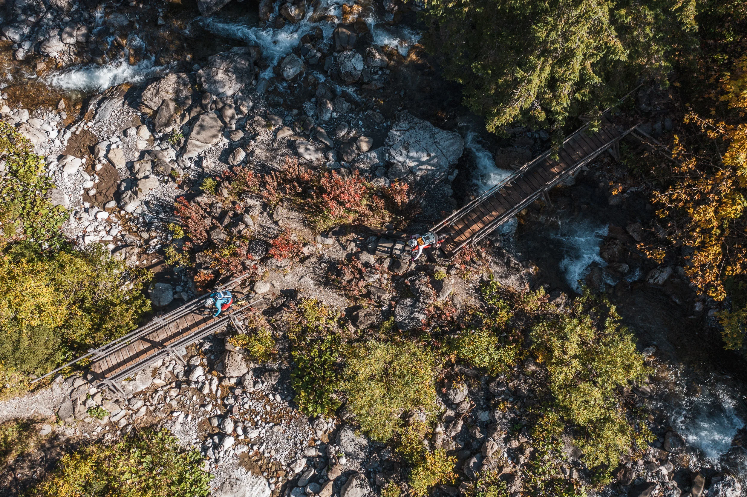 Zwei Mountainbikerinnen auf einer Holzbrücke zwischen Felsen und Herbstwald