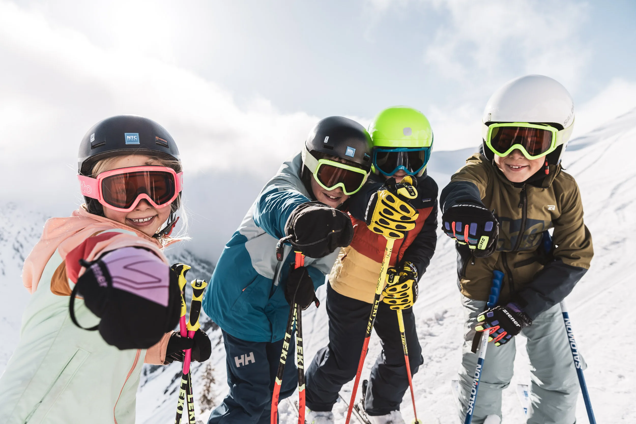 Vier Kinder und ein Skilehrer posieren lachend auf der Piste
