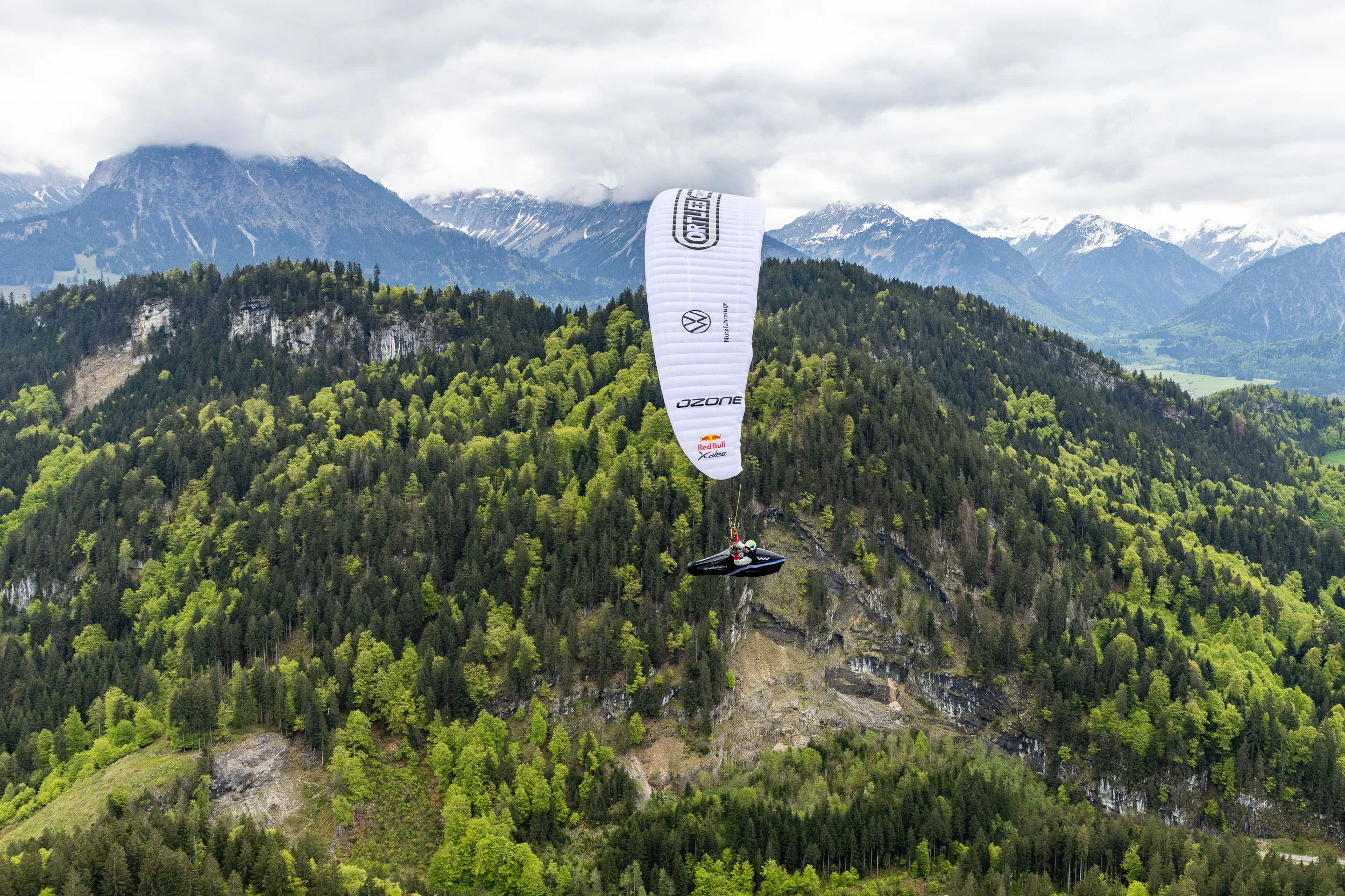 Eli Egger gleitet mit ihrem Gleitschirm vor bewaldeten Bergen im Allgaeu.