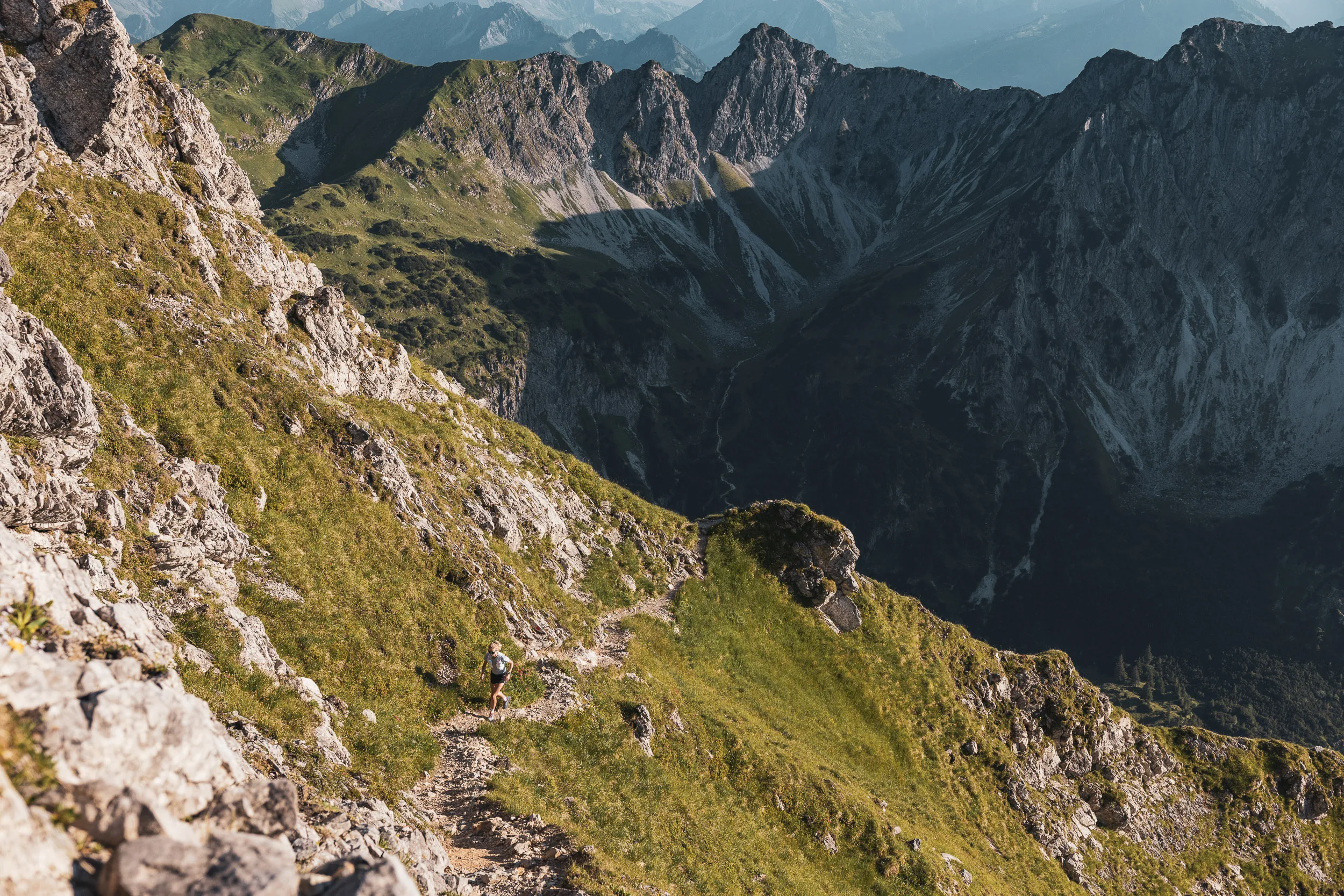 Steiniger Bergpfad entlang eines steilen Hangs vor dunkler Felskulisse