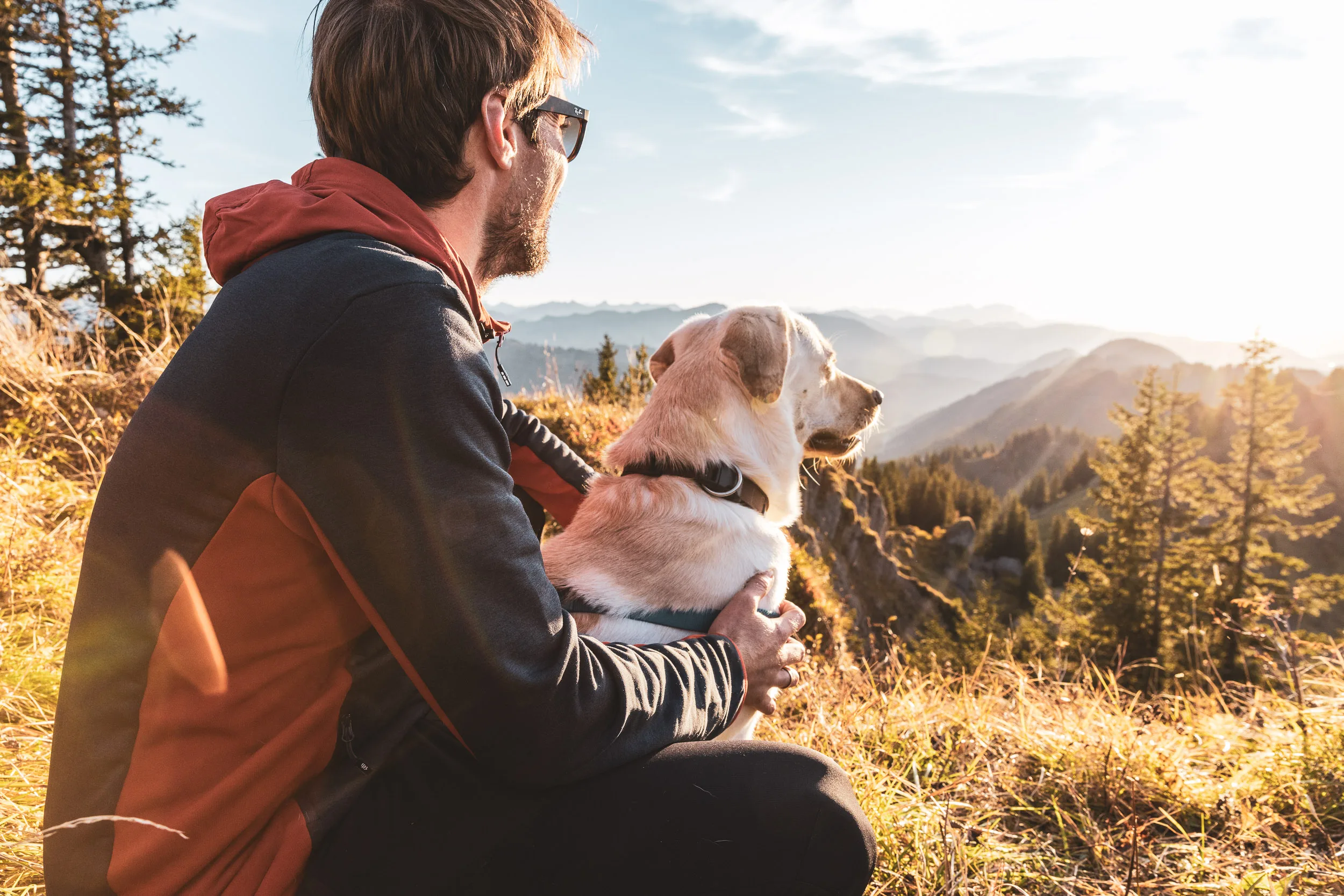 Andreas Kögel sitzt mit Hund Oskar auf einer Bergwiese und blickt über das Oberallgäu