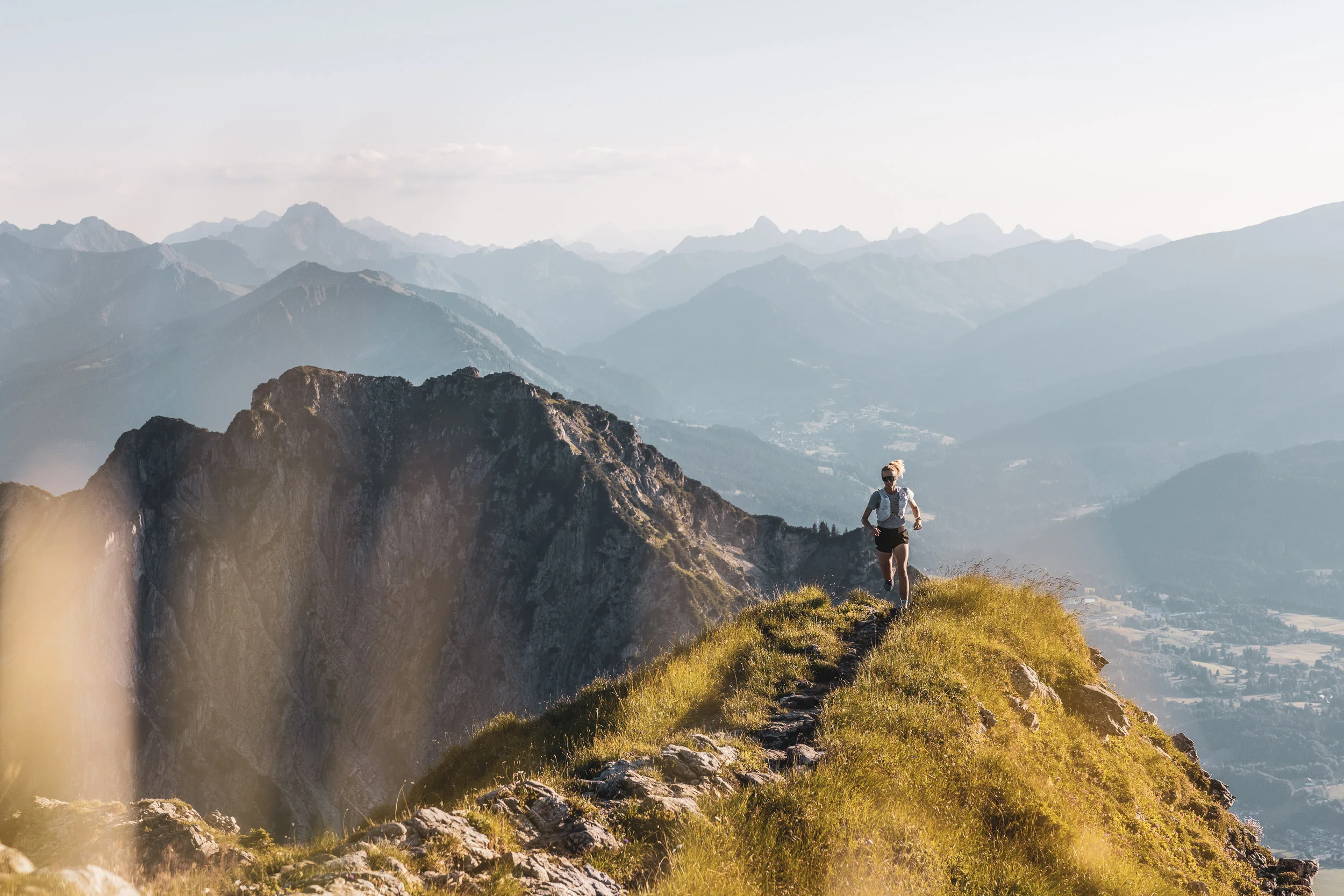 Trailrunnerin im warmen Abendlicht auf einem grasbewachsenen Berggrat