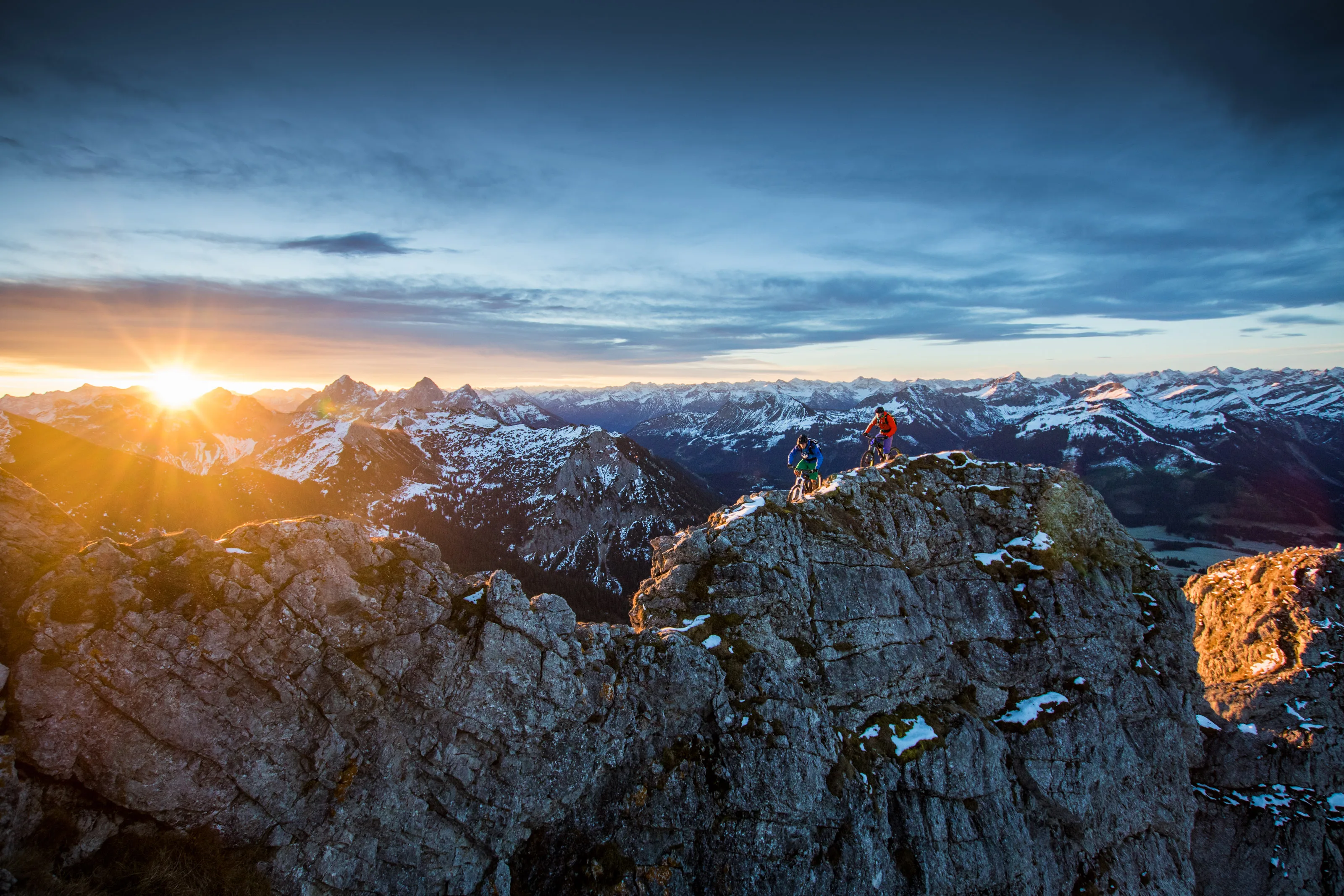 Florian Häusler und Robert Härle mit Mountainbikes auf einem felsigen Grat im Morgenlicht.