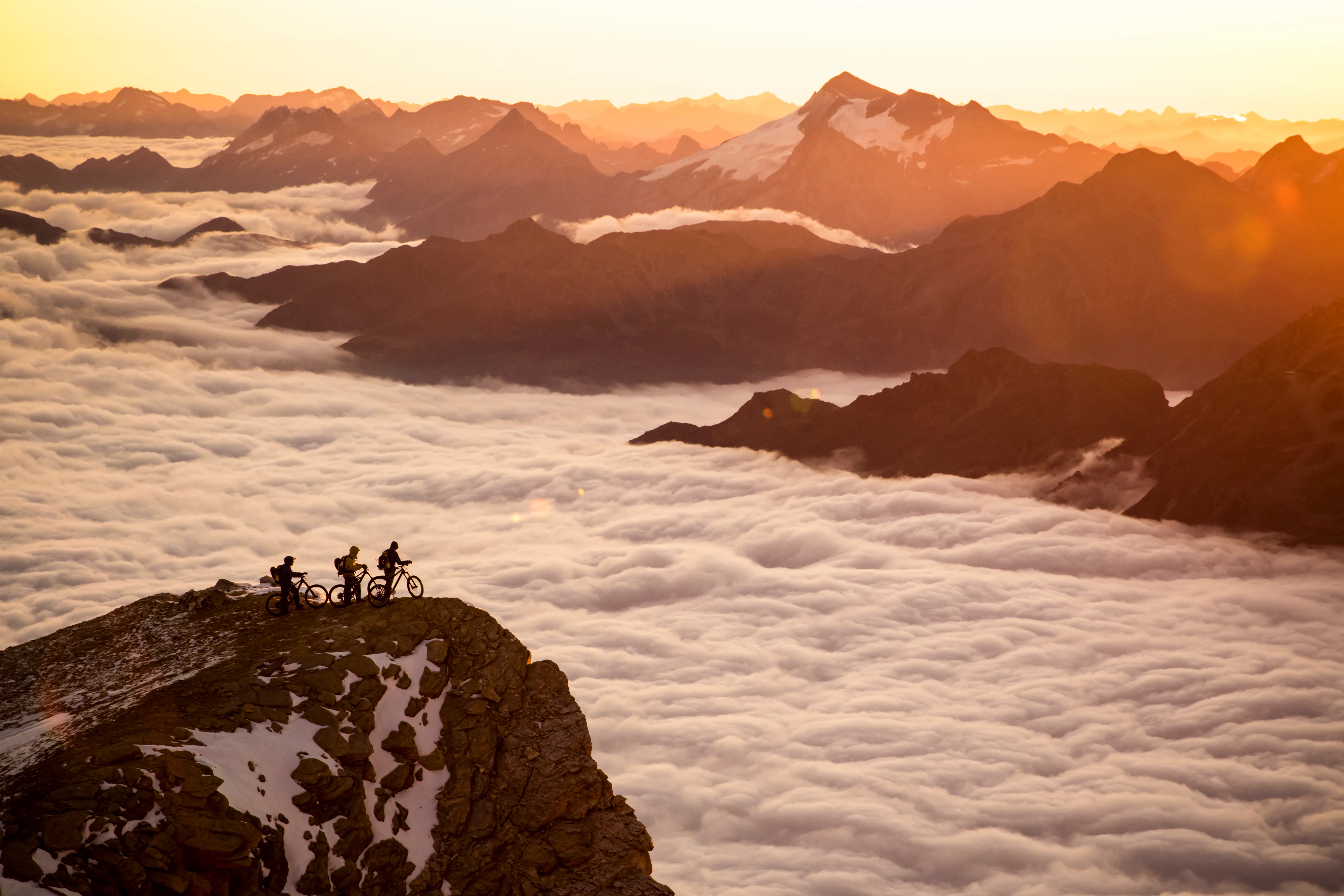 Mountainbiker zeichnen sich als Silhouetten vor dem Morgenlicht über dem Wolkenmeer ab.