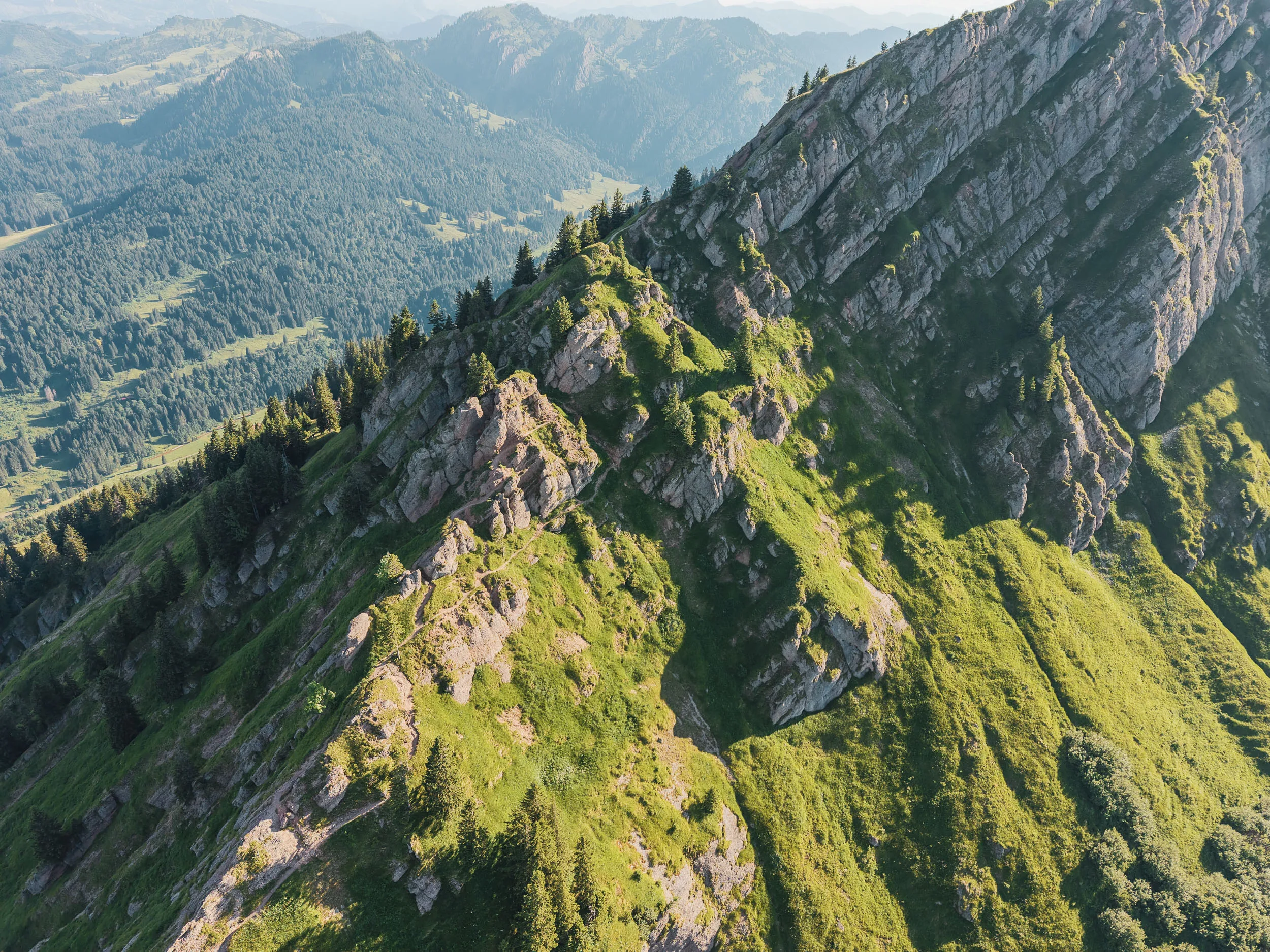 Ein schmaler Pfad zieht sich zwischen Felstürmen und grünen Hängen über einen Berggrat.